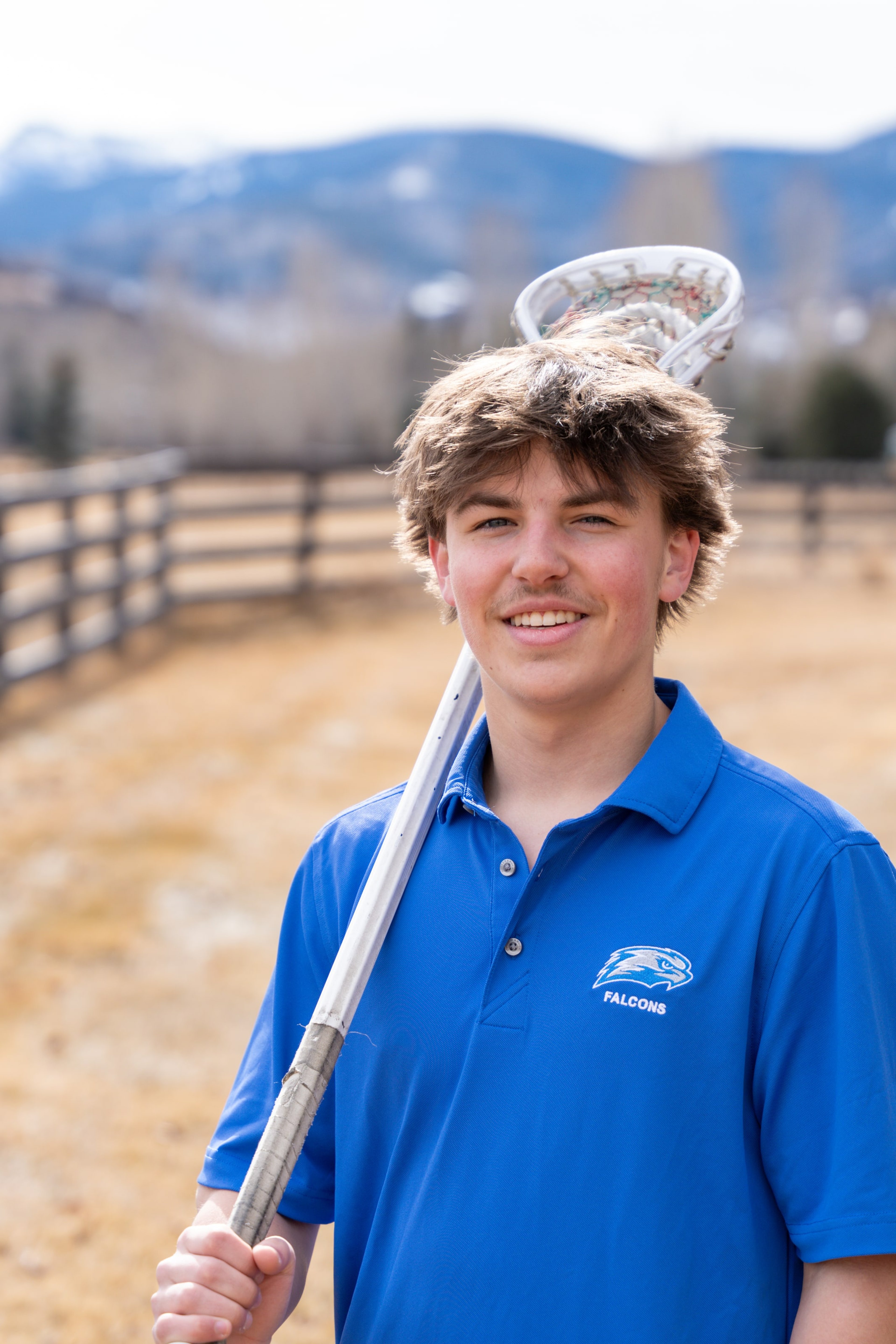 Teagan with a lacrosse stick across his shoulders, grinning