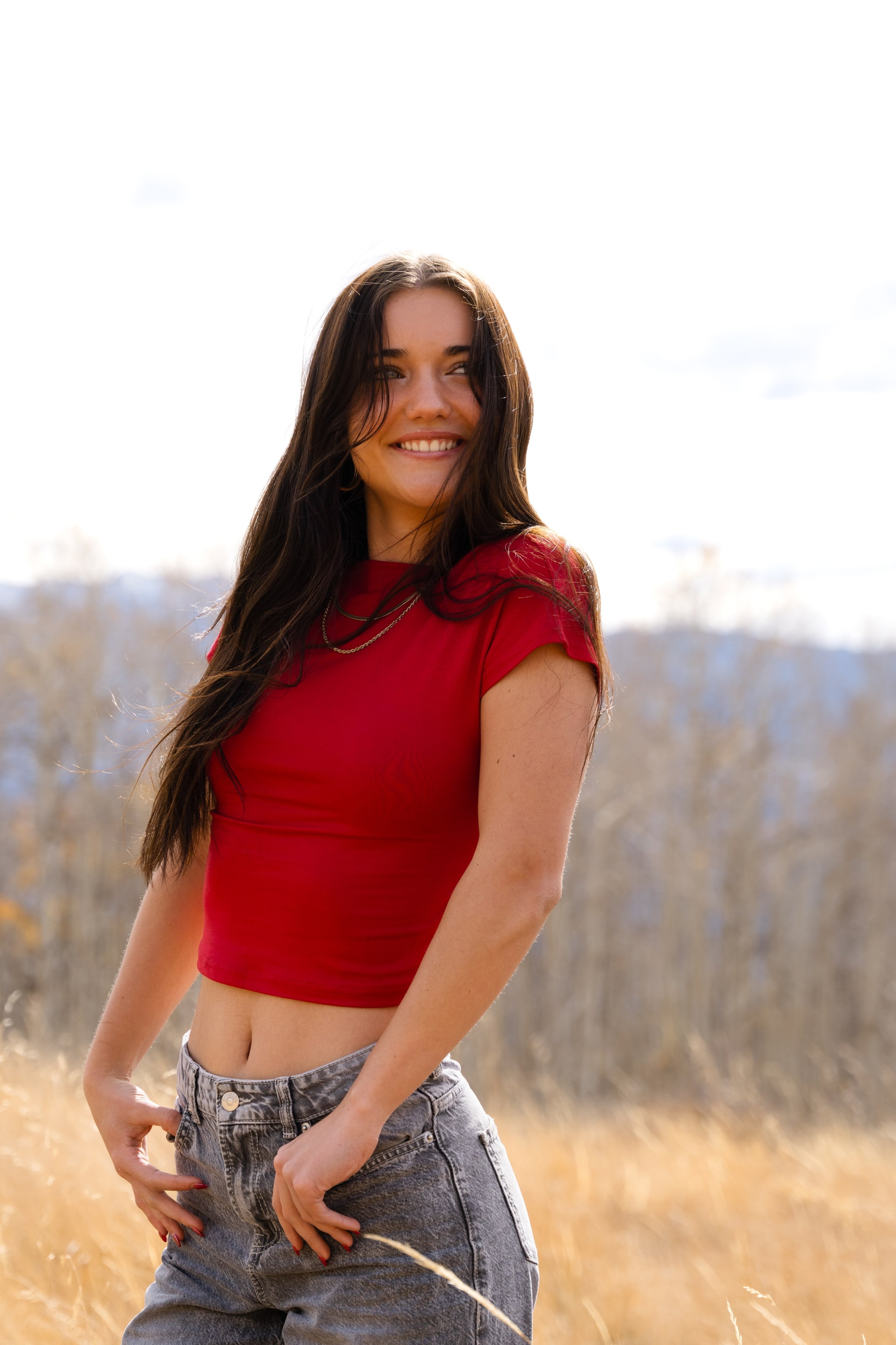 Lucy in a red top, wind in her hair, smiling in evening light
