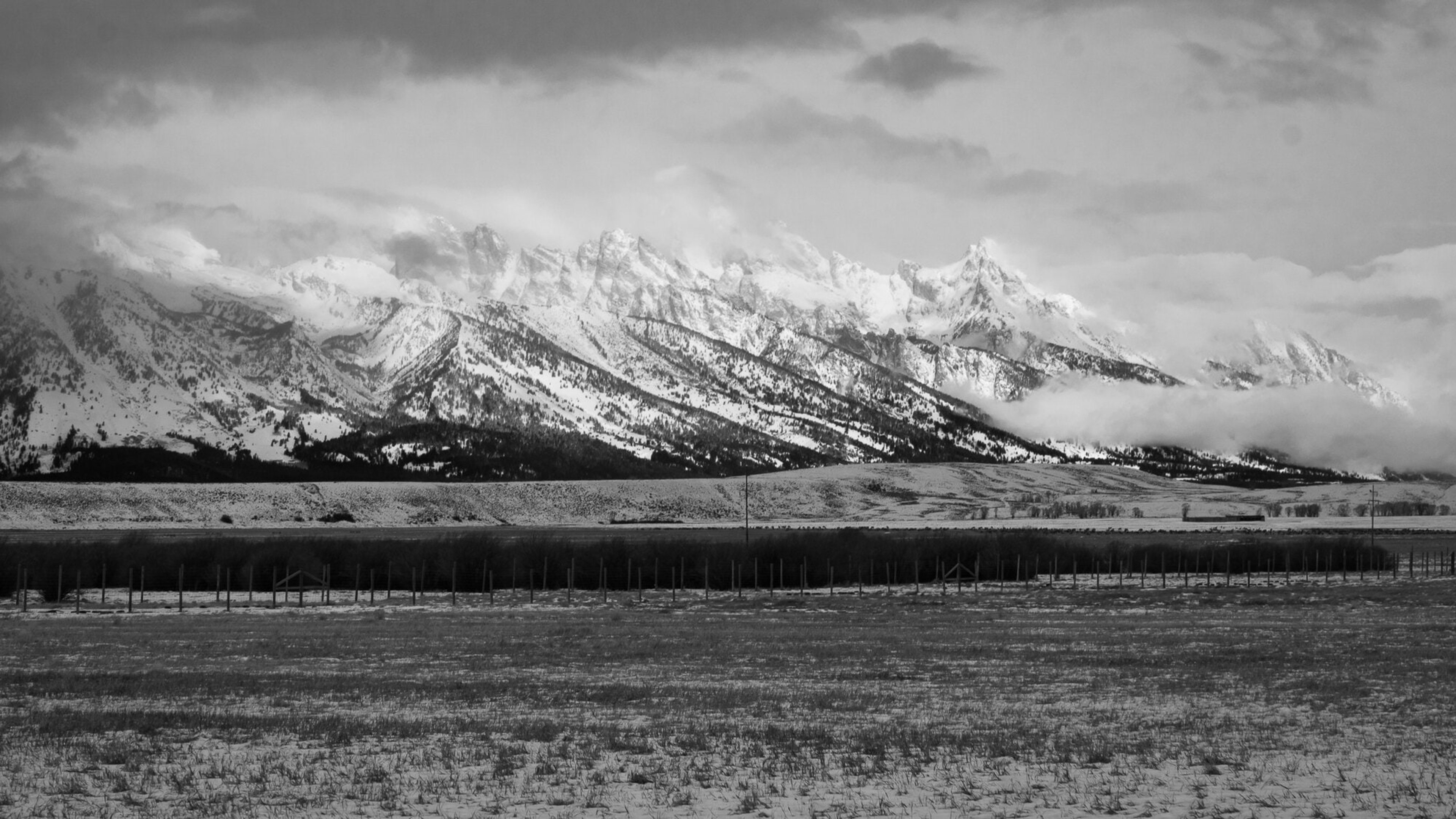 The Grand Teton range under a heavy sky above a bare winter plain, in black and white