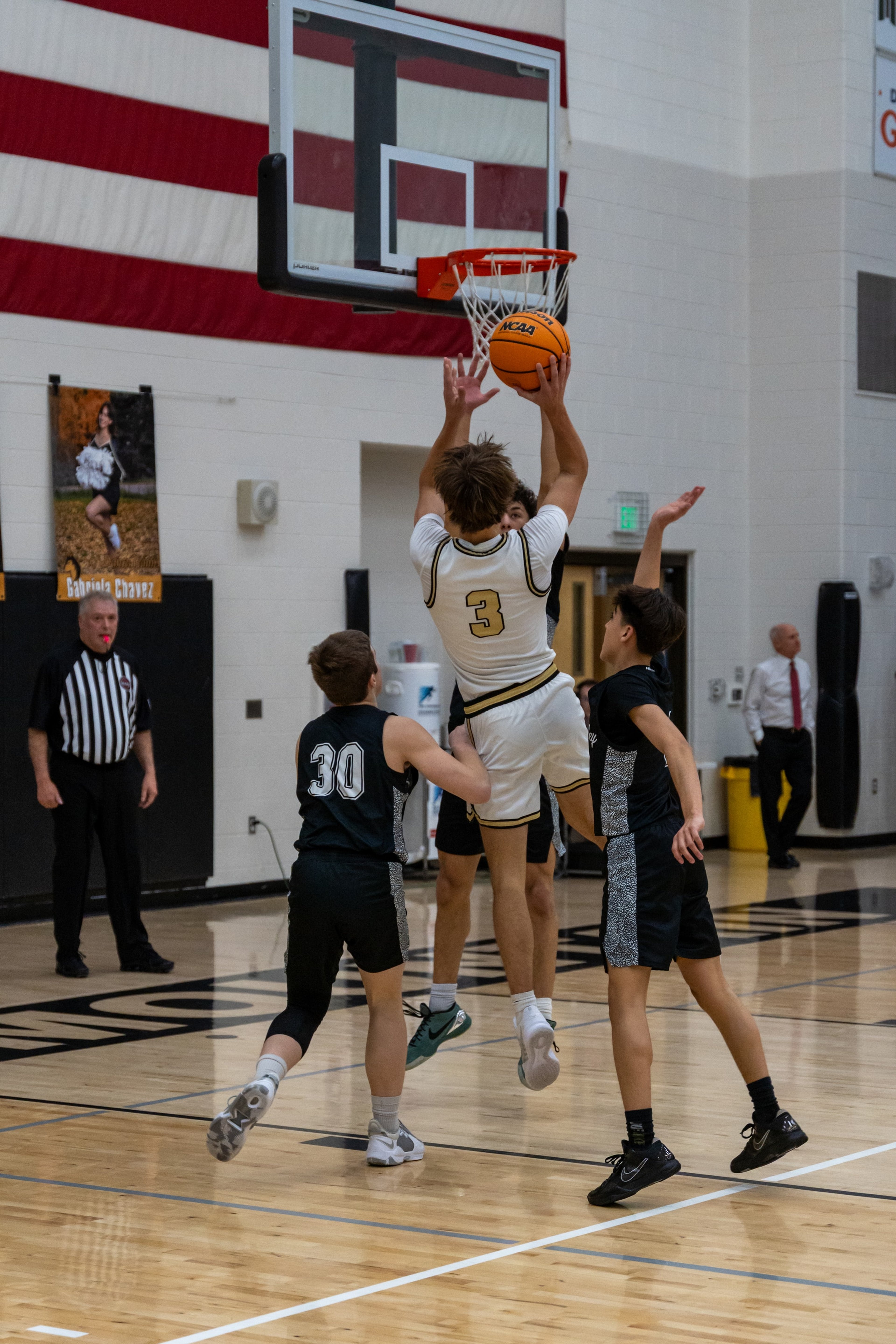 A player reaches for the rim between two defenders