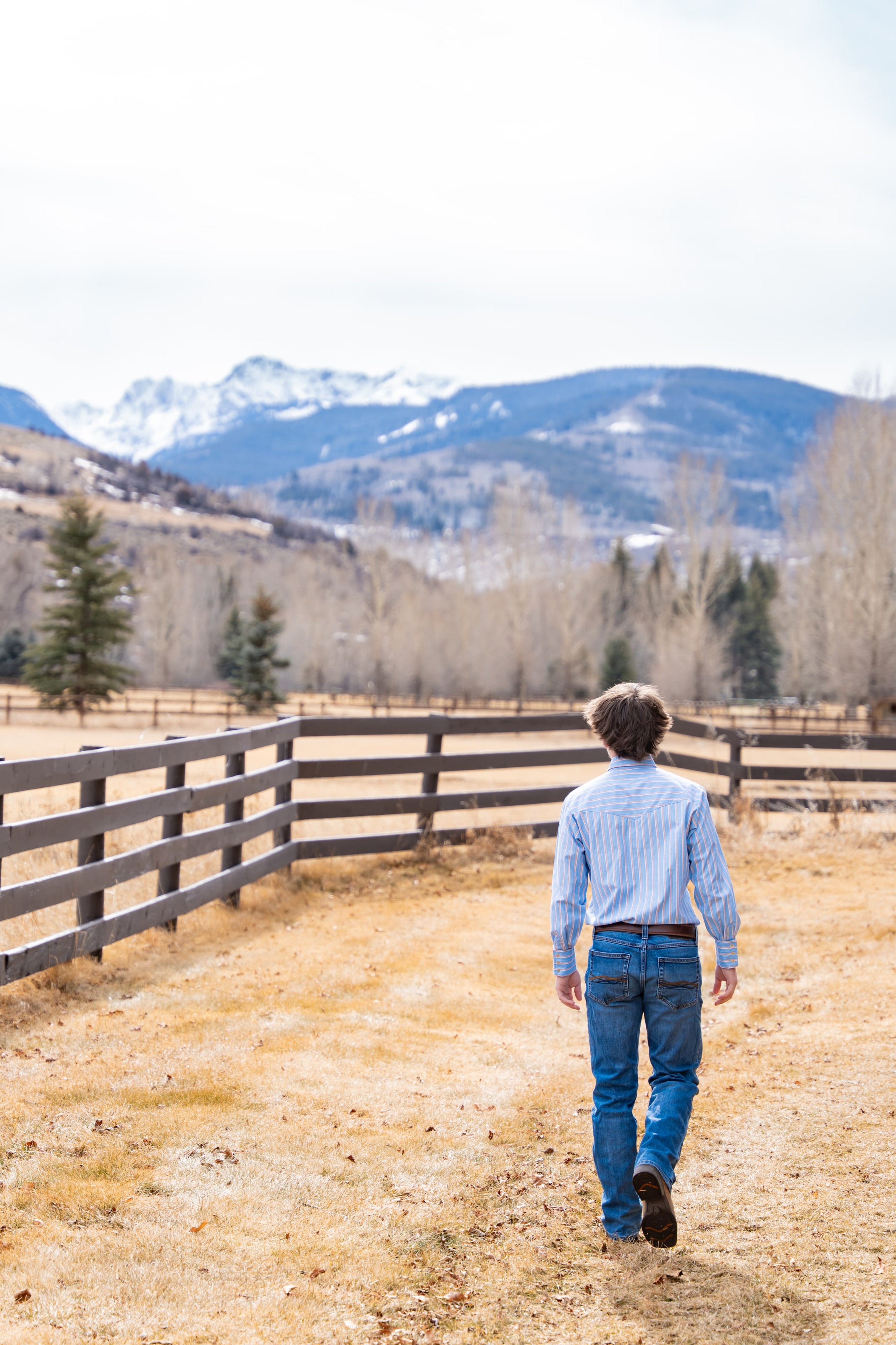 Teagan walking away down a ranch fence line toward snowy peaks