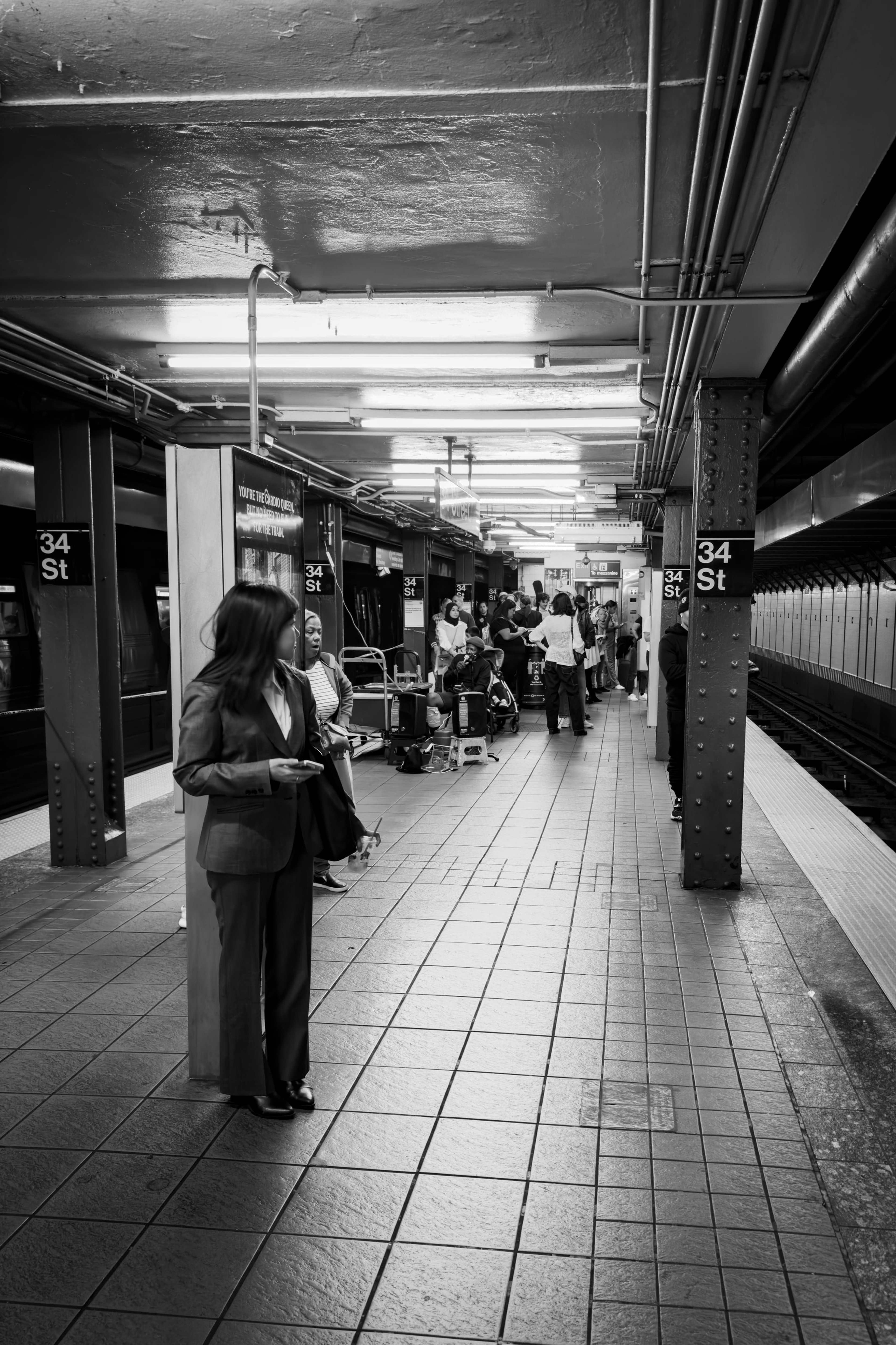 A woman waiting on a New York subway platform as the corridor recedes to a vanishing point, in black and white