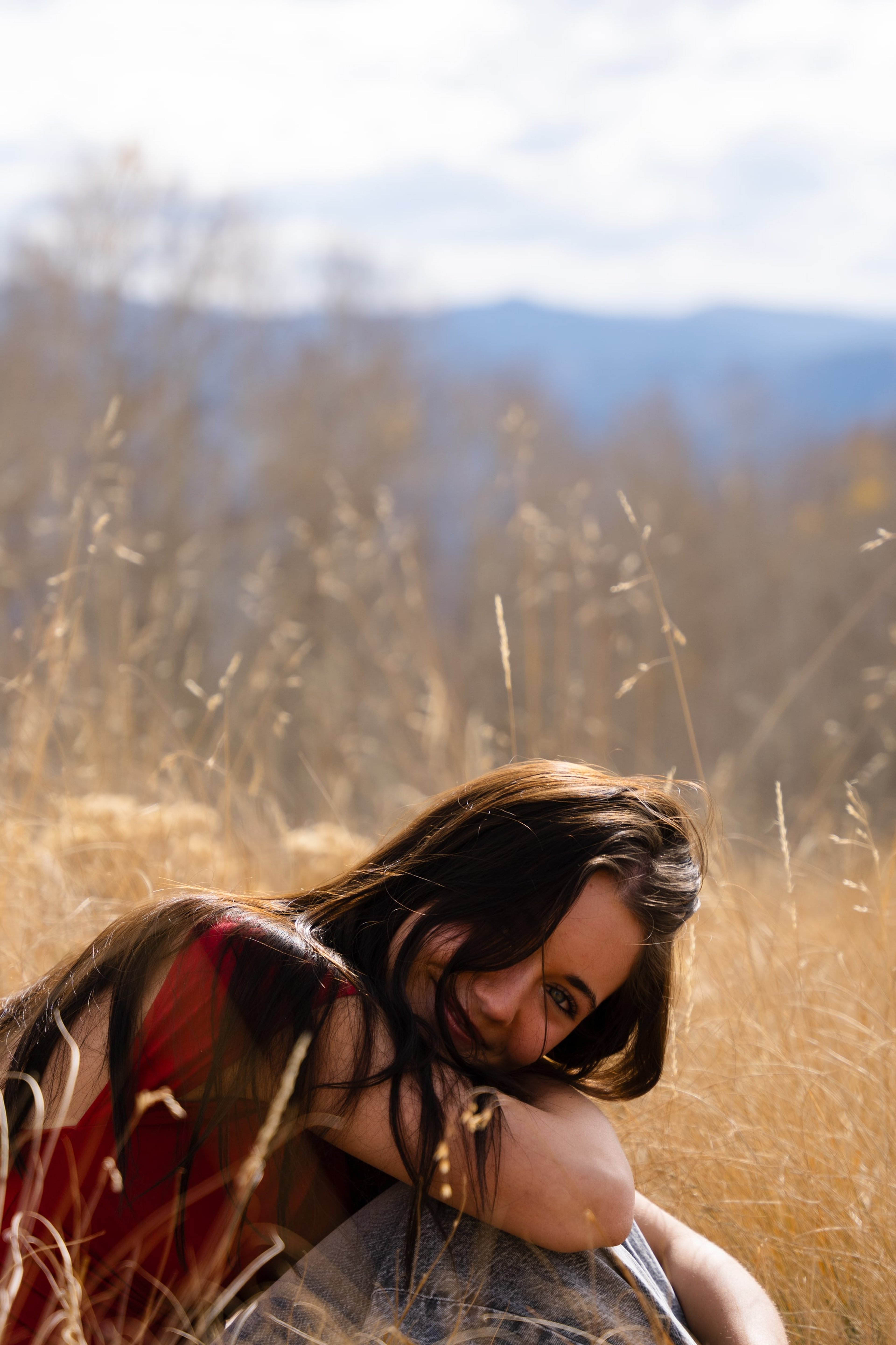 Lucy lying in tall golden grass in a red top, mountains soft behind