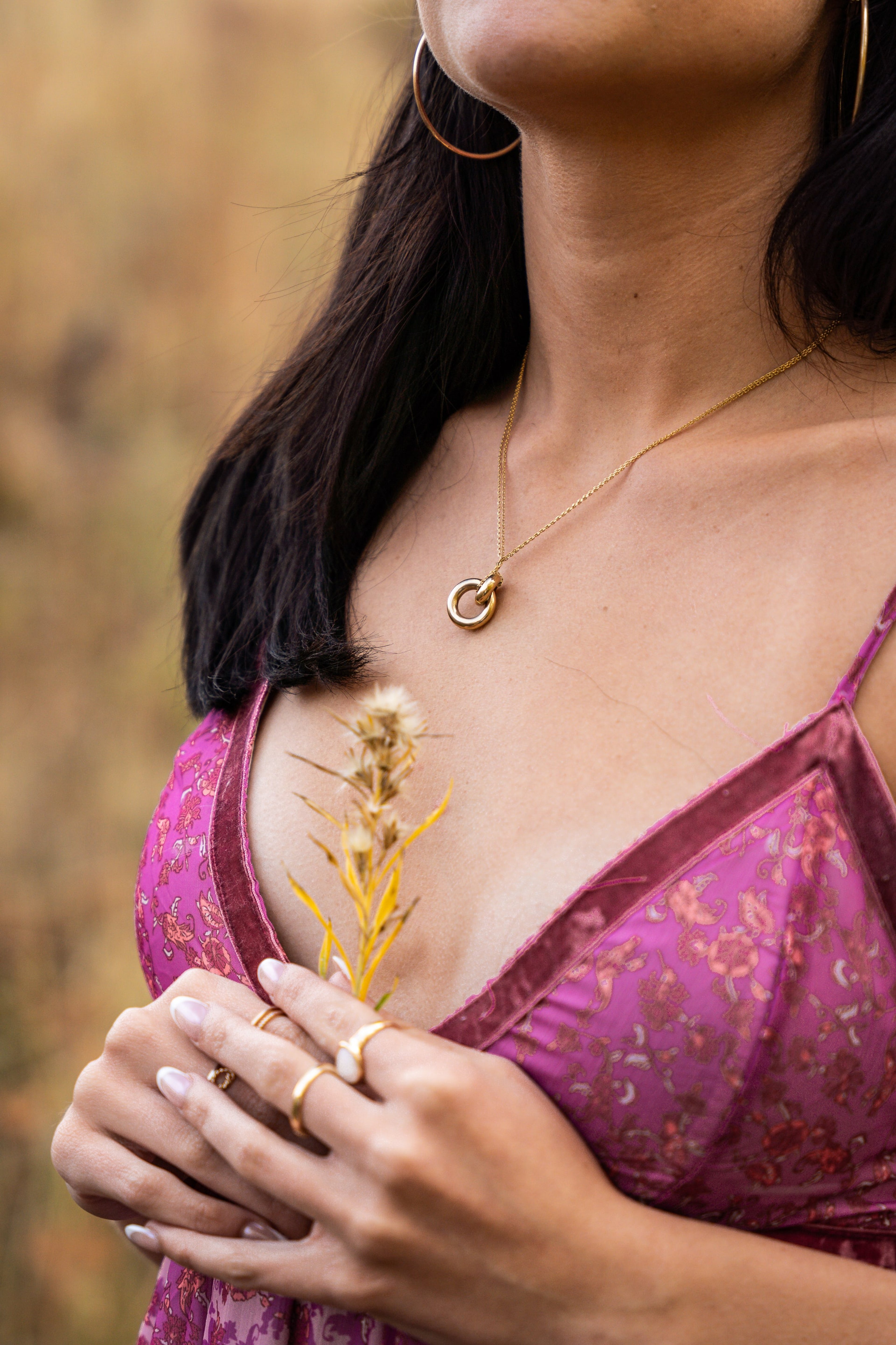 Detail of a gold necklace and wildflower stem held against a magenta dress