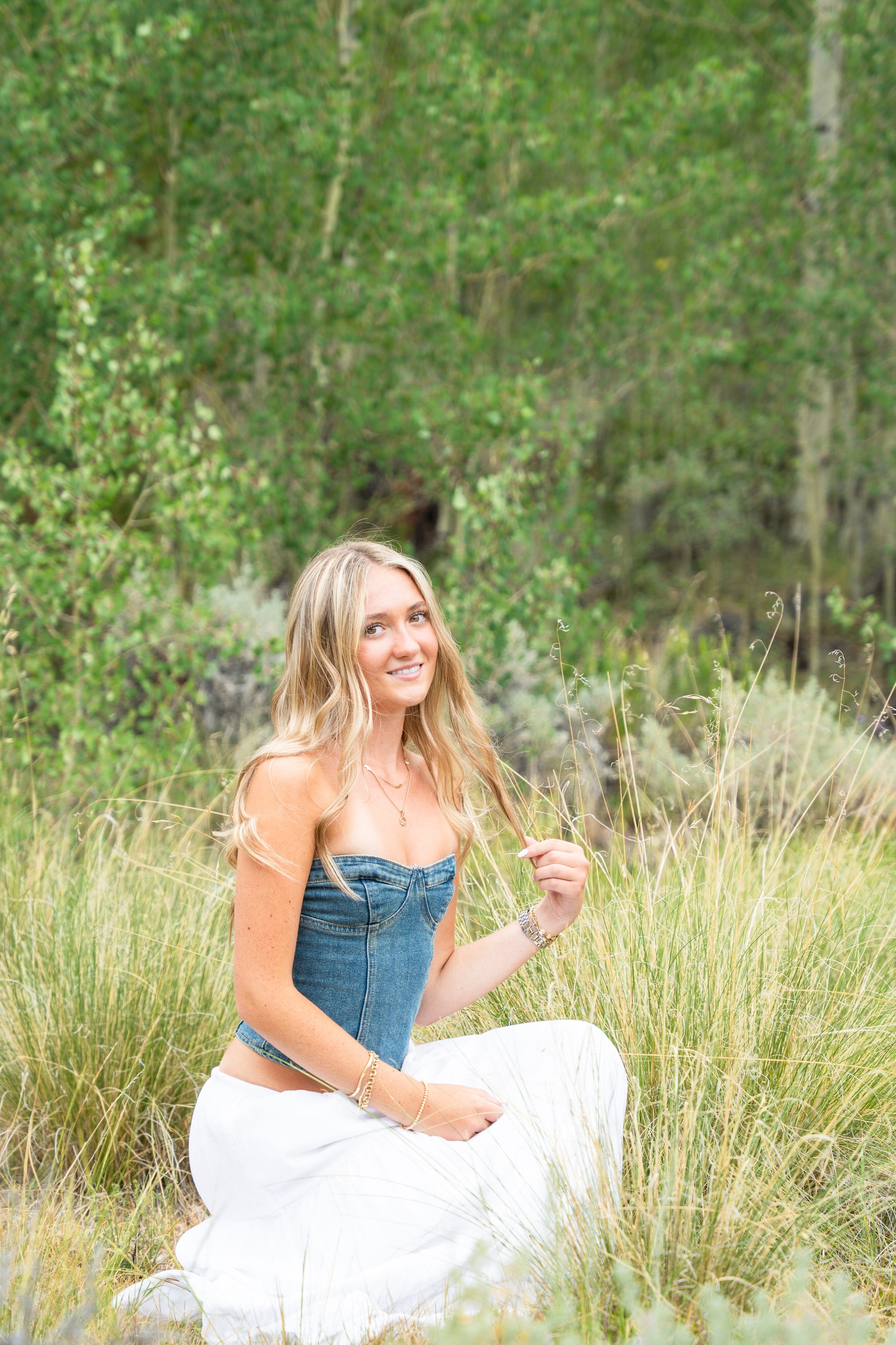 Caleigh in a blue top and white skirt holding a stem of grass