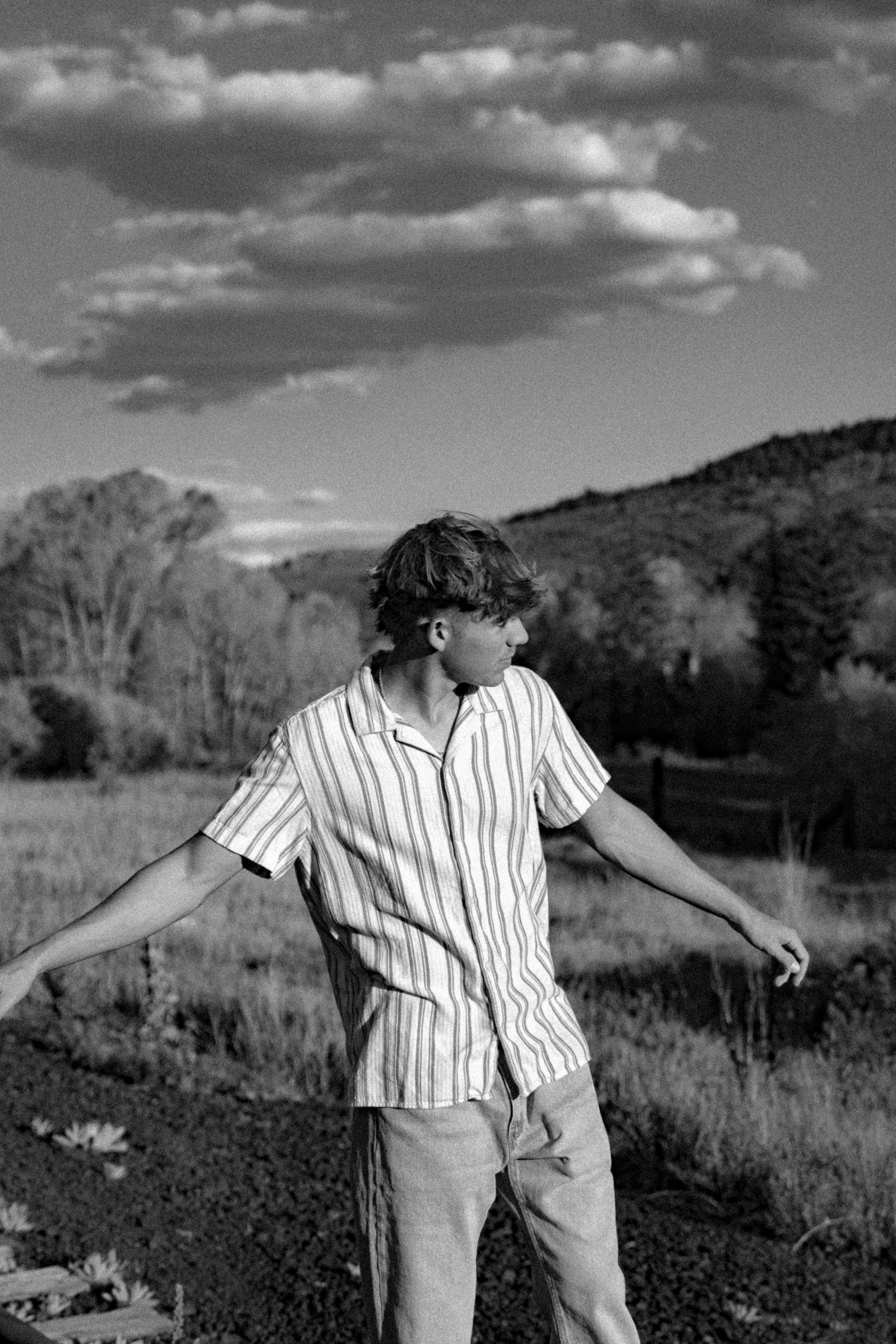 Wyat with arms out in a field under big clouds, in black and white