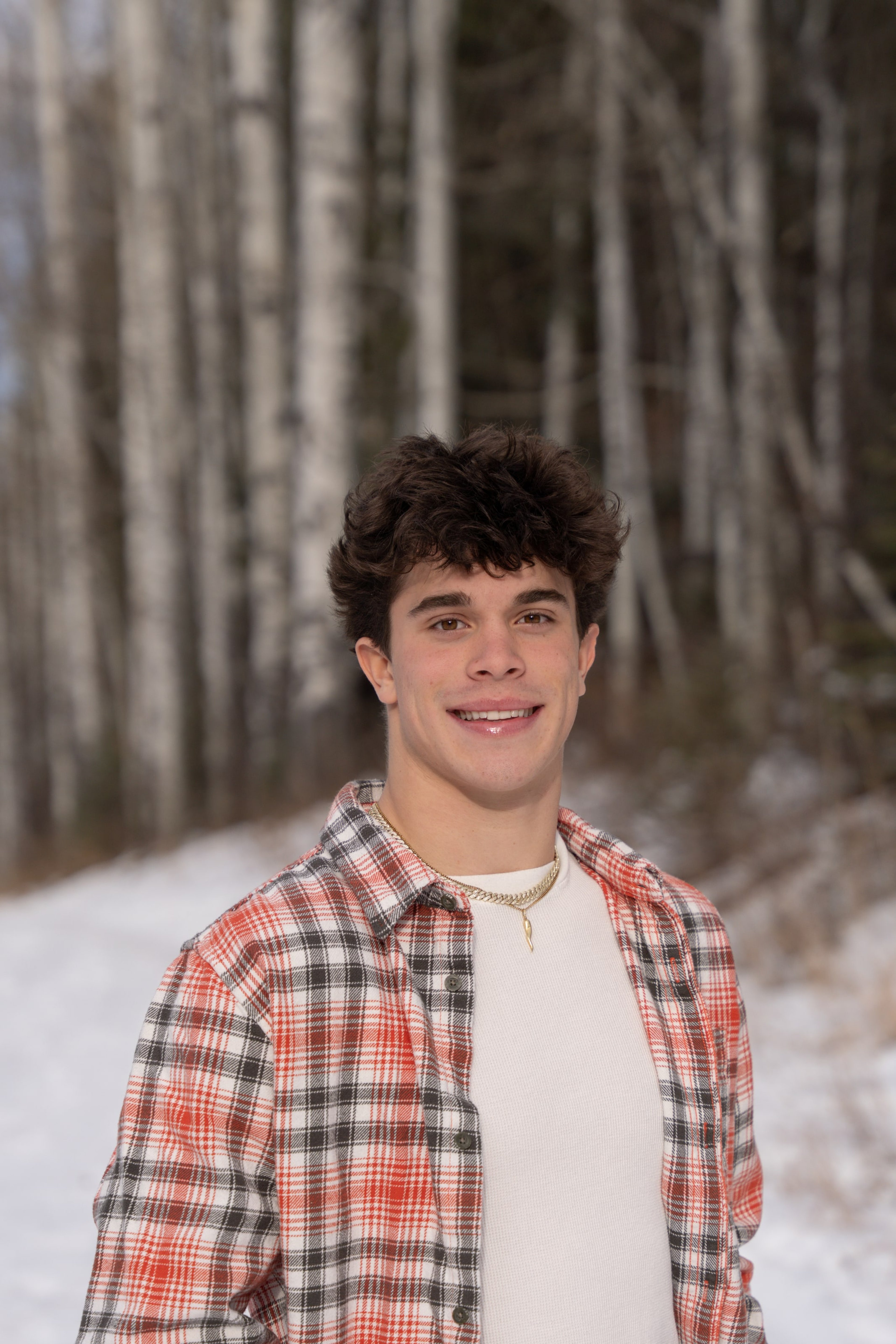 Ryder smiling in plaid, snow in the trees behind