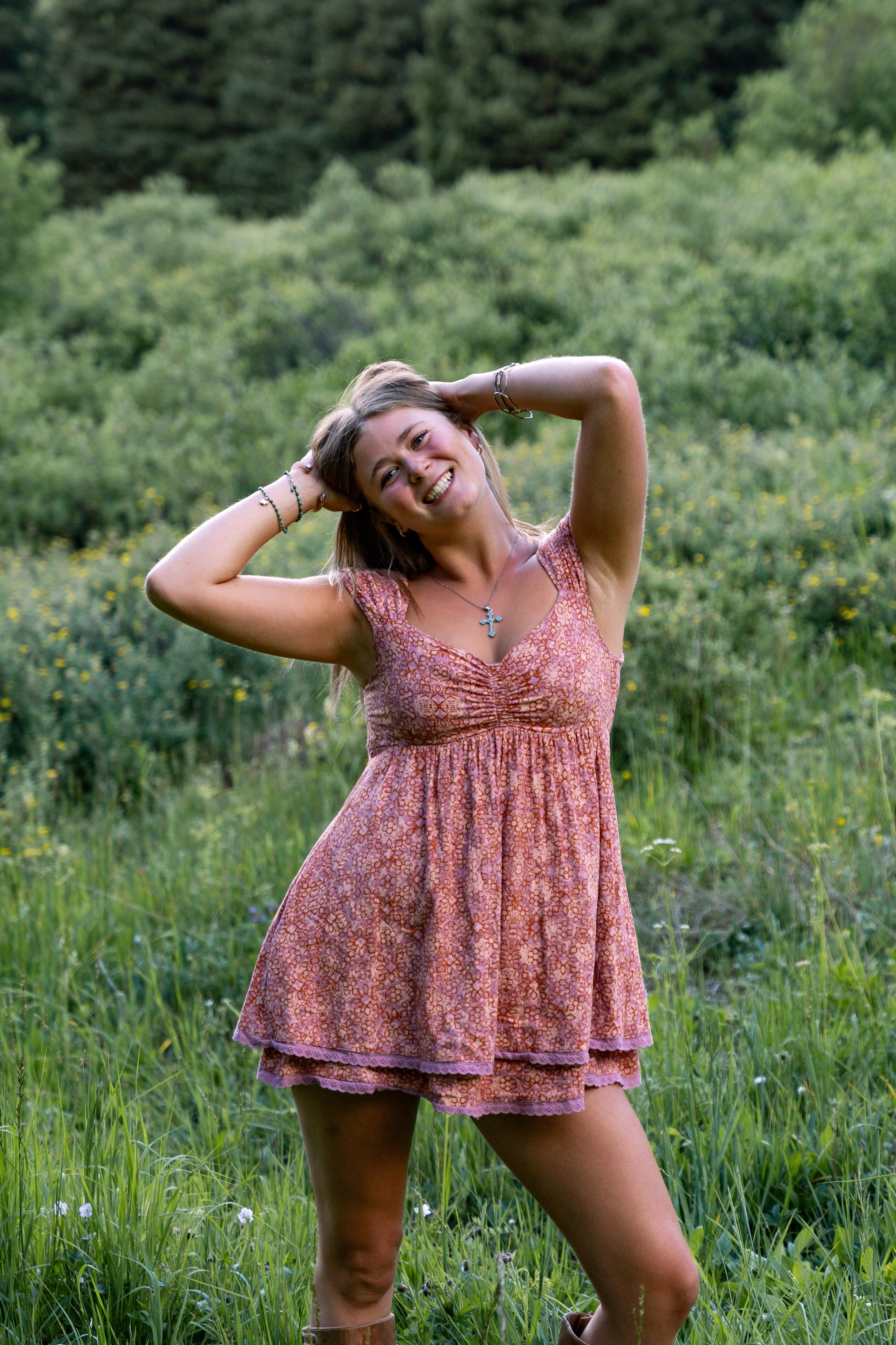 A girl in a pink dress, hand in her hair, smiling in the meadow