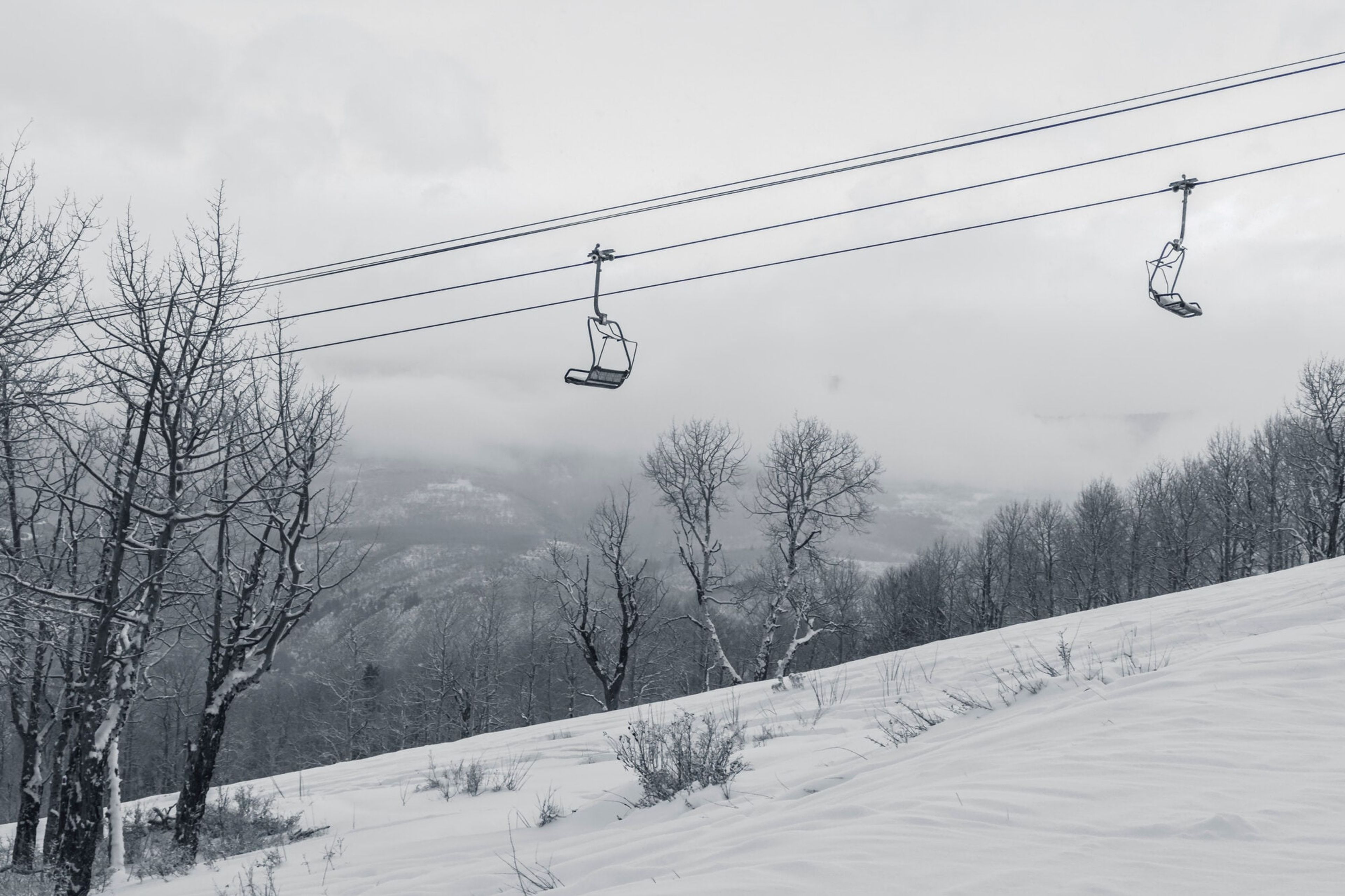 An empty chairlift disappearing into snowfall and fog above a silent run