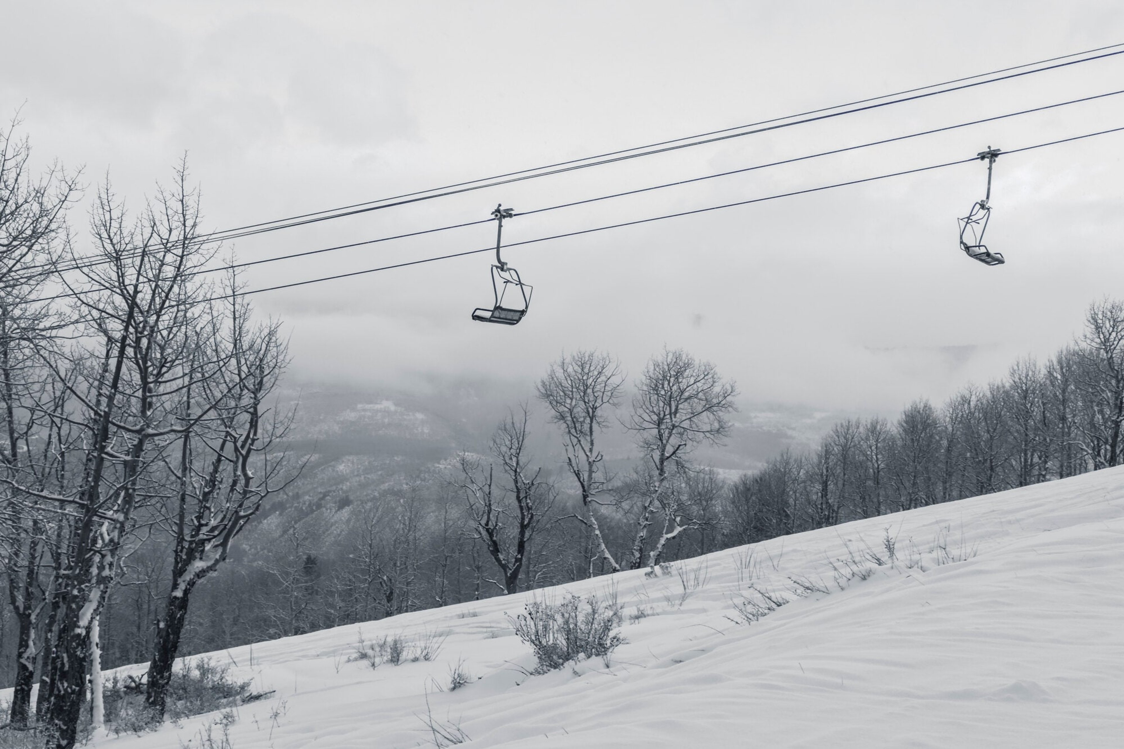 An empty chairlift disappearing into snowfall and fog above a silent run