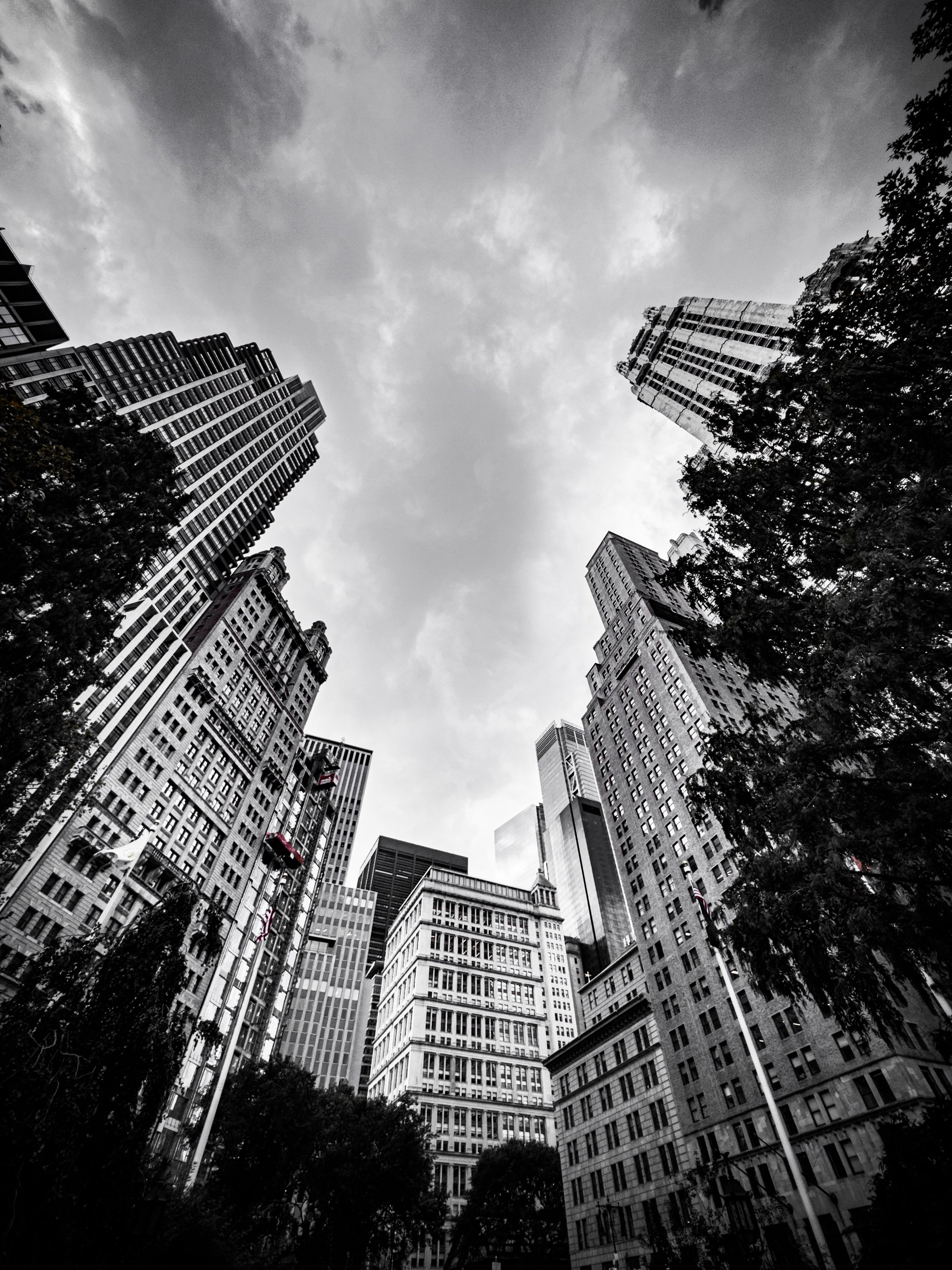 Manhattan towers shot straight up from the street, converging into a bright sky, in black and white