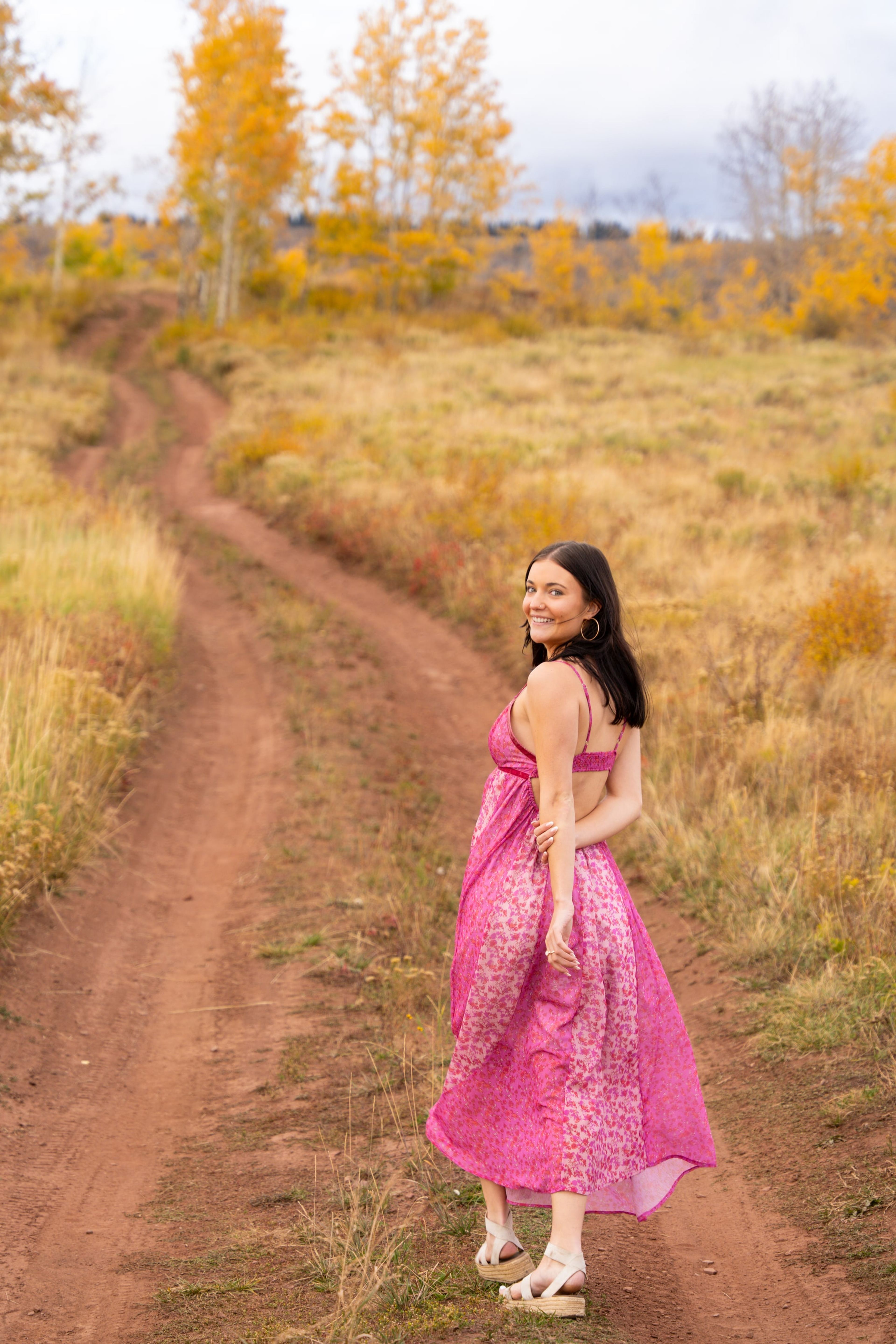 Lucy in a pink dress glancing back on a red dirt road through golden aspens