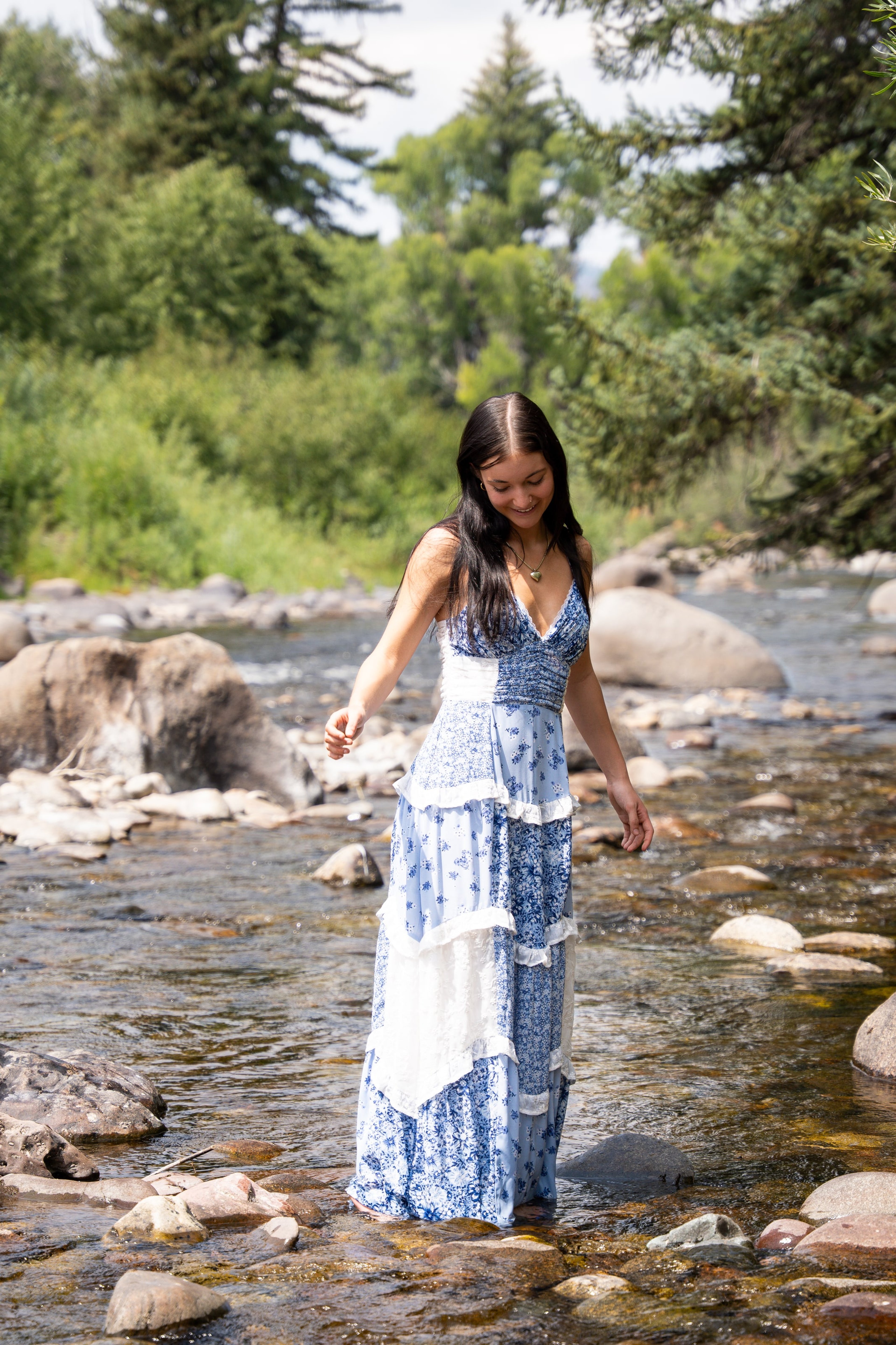 Lucy in a blue patchwork dress stepping across a rocky mountain creek
