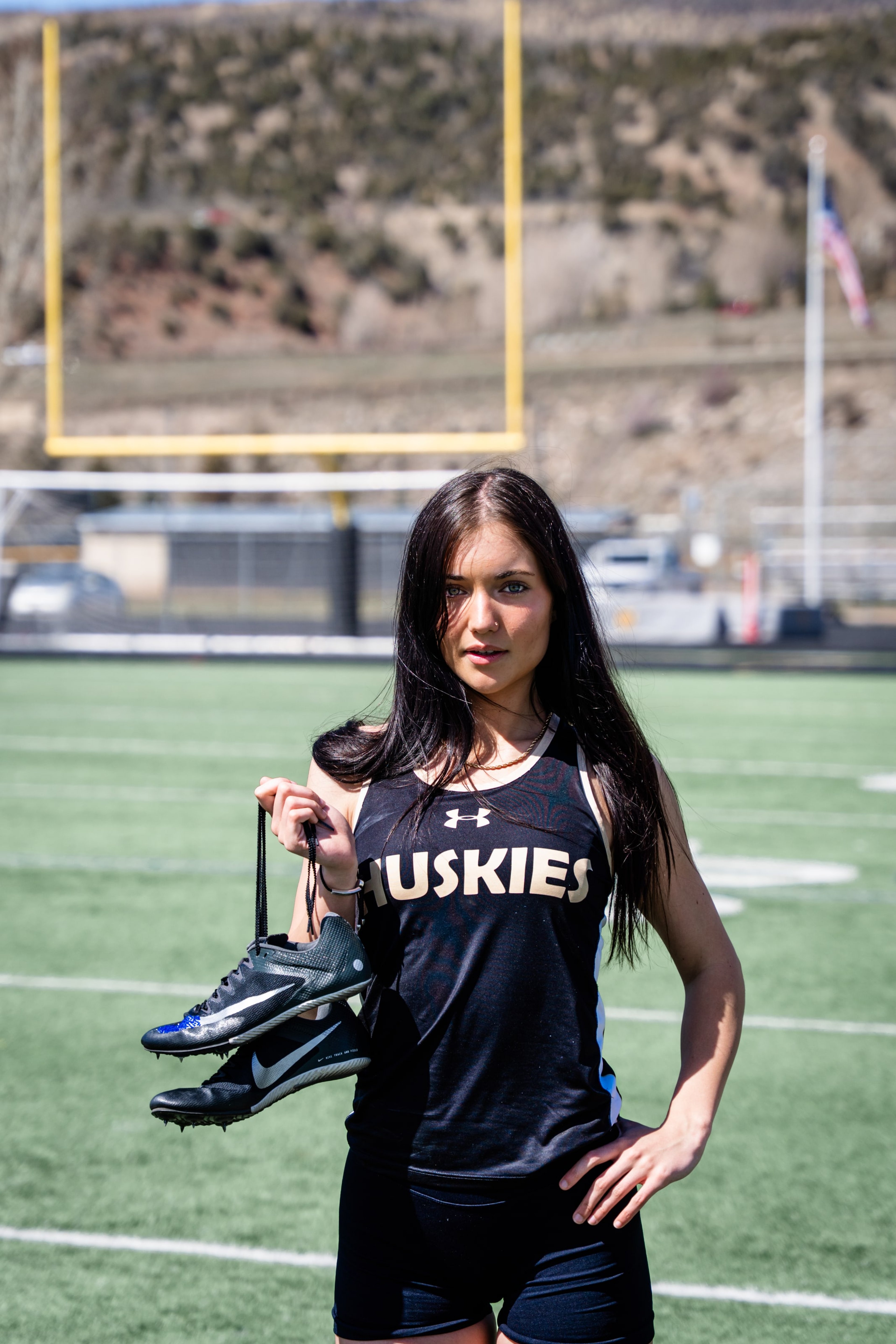 Lucy on the field with spikes in hand, flag on the hill behind