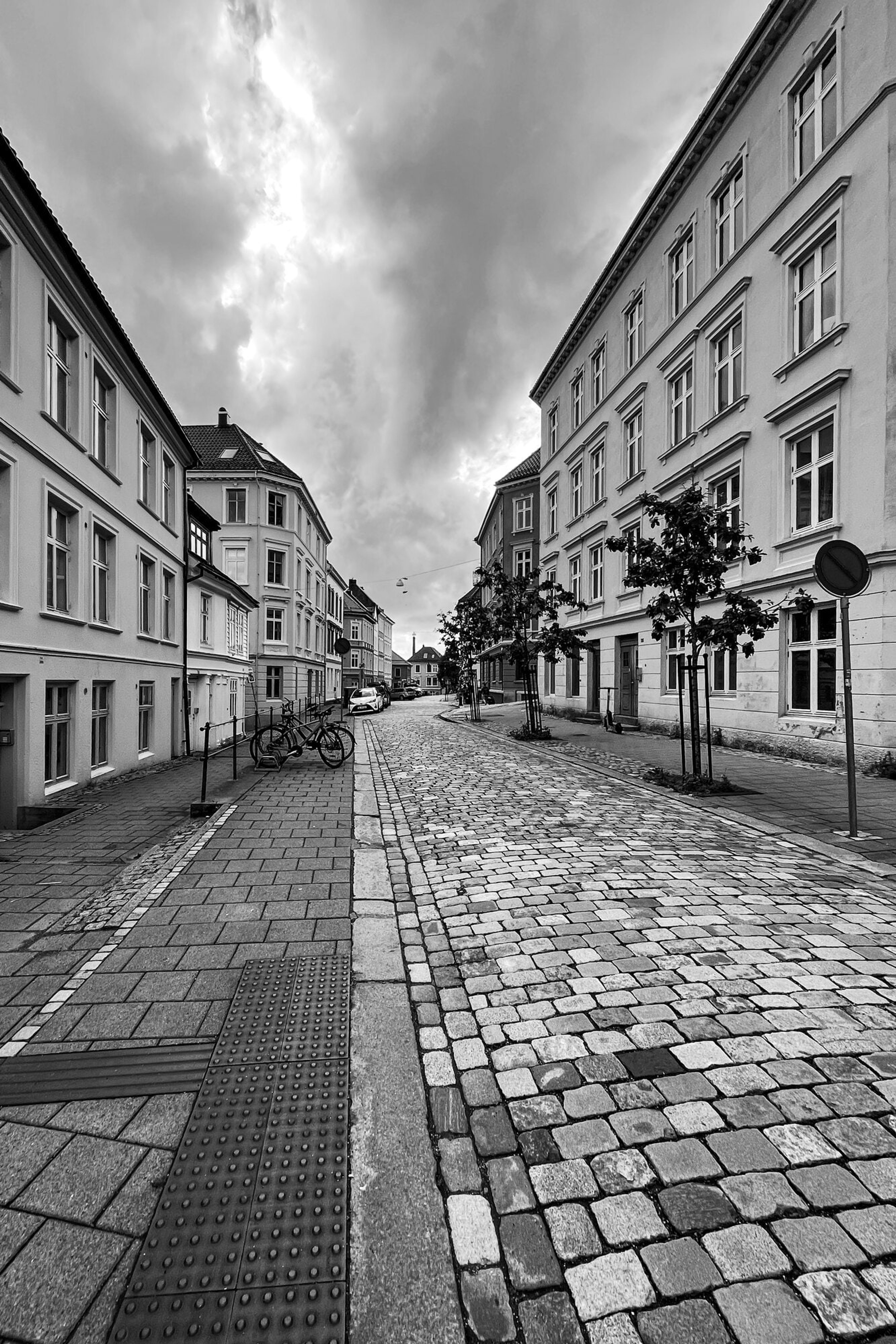 A cobbled Bergen street drawing to a vanishing point between old facades, in black and white