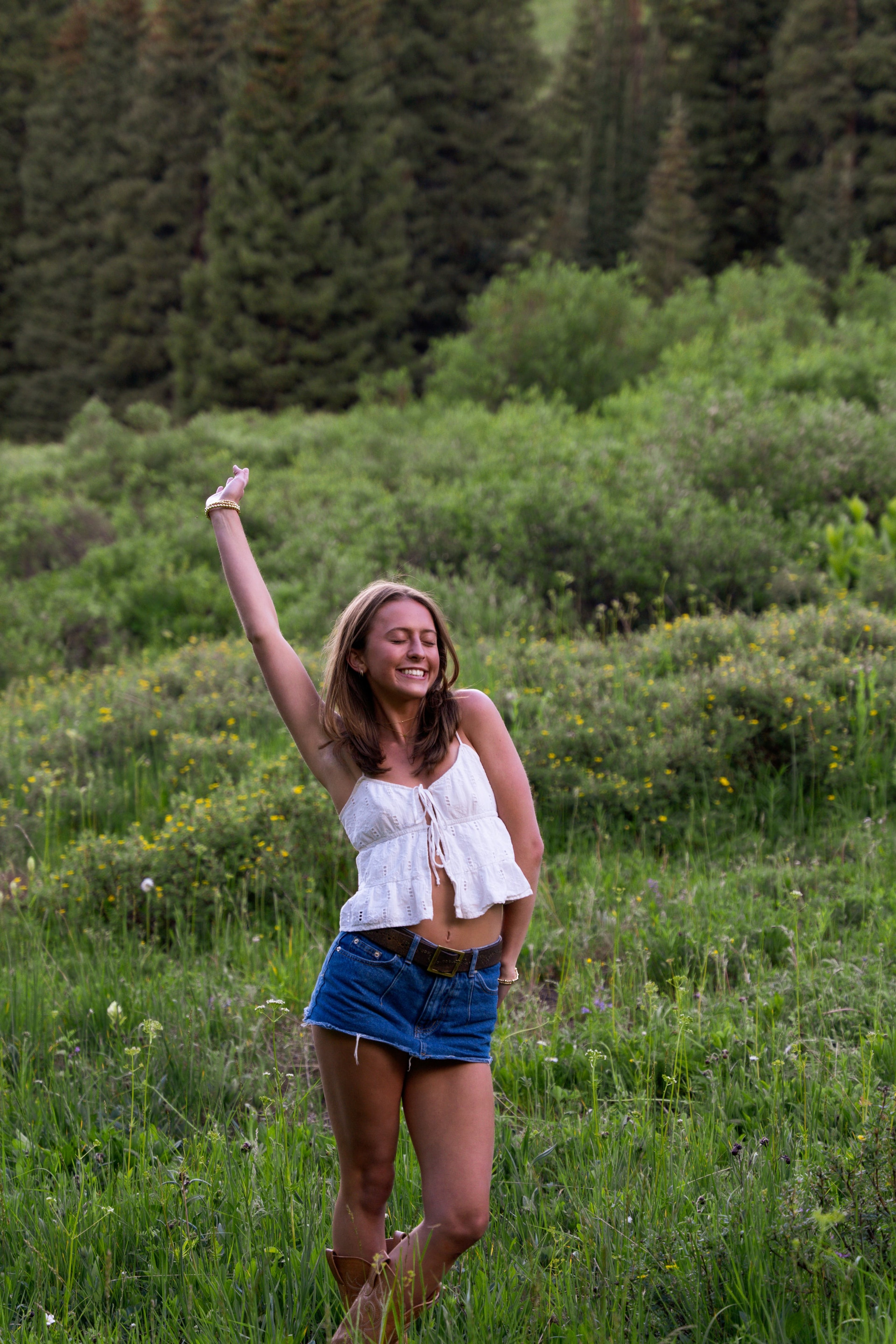 A girl in white with an arm raised, meadow rolling behind