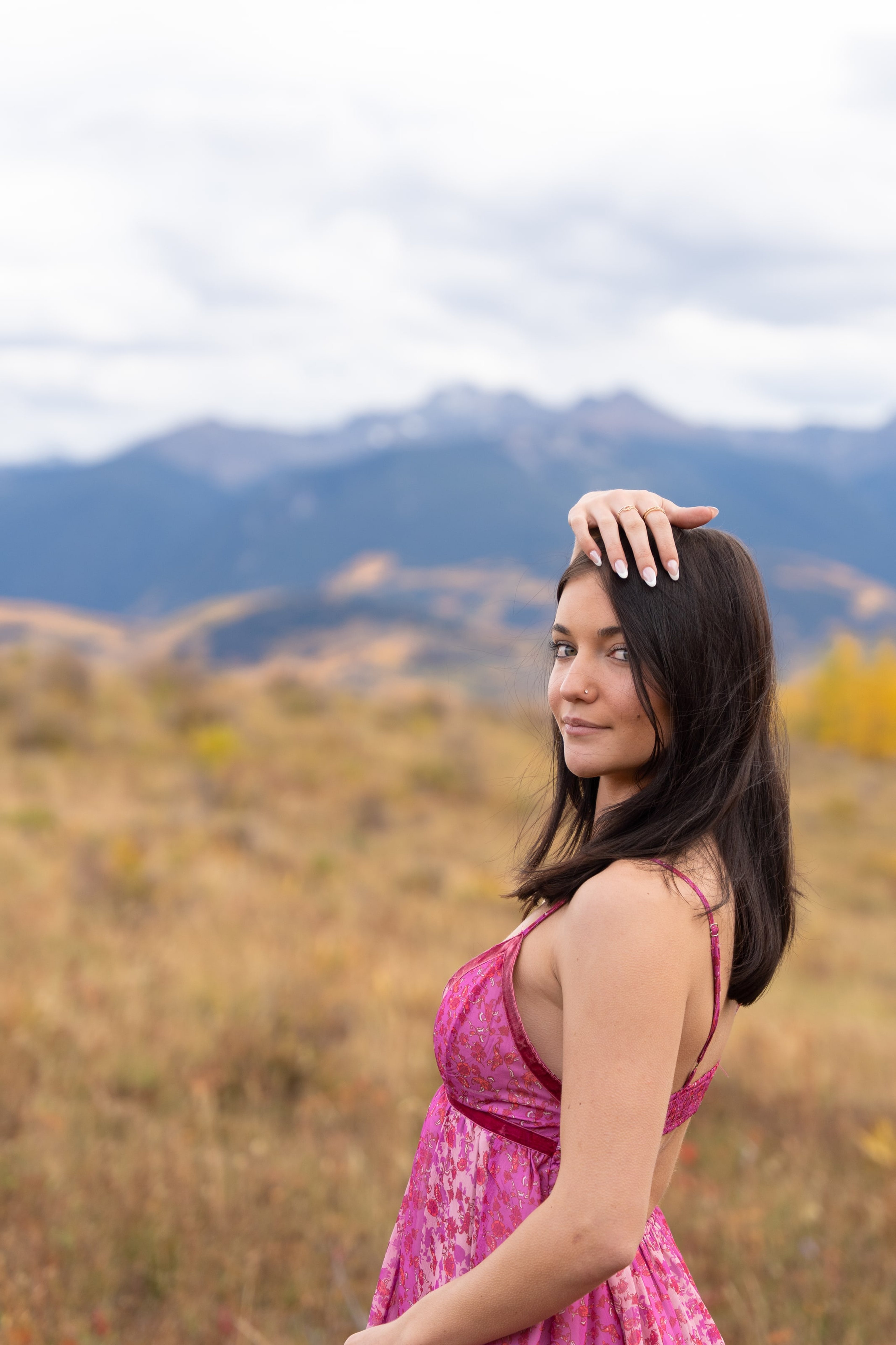 Lucy in a pink dress, hand in her hair, peak on the horizon