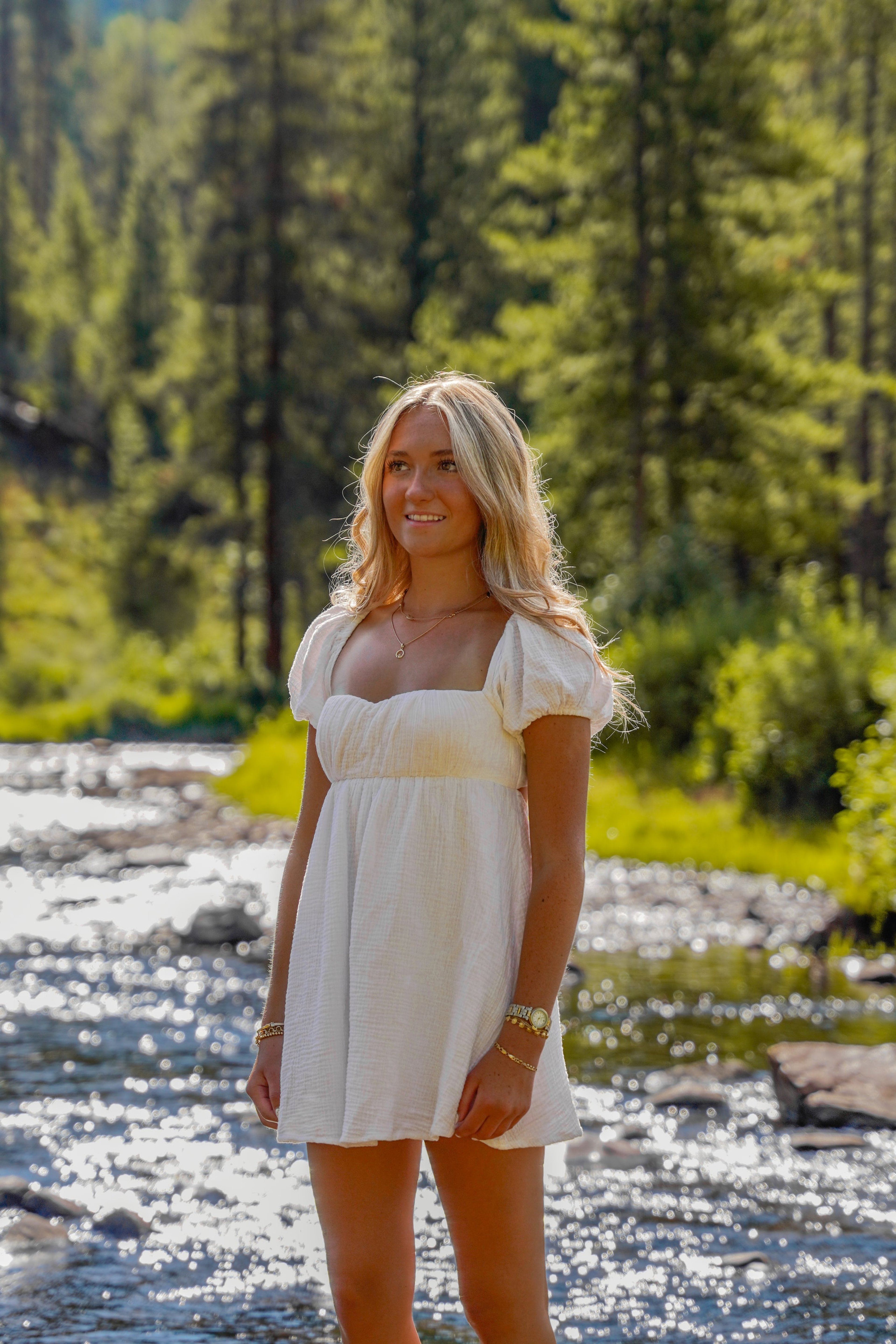 Caleigh smiling beside a sunlit mountain stream