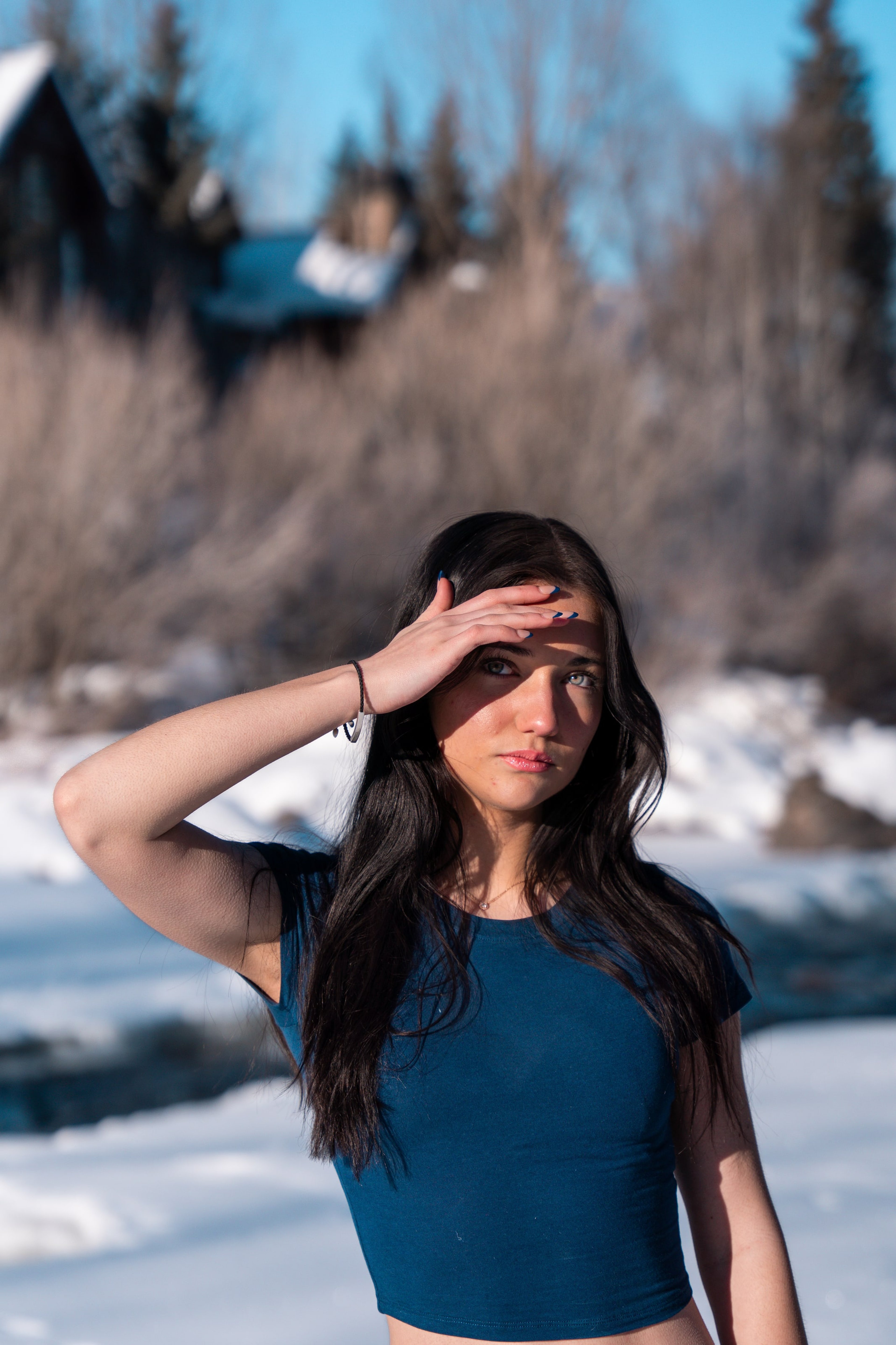 Lucy squinting into bright snow-light, hand raised, river behind