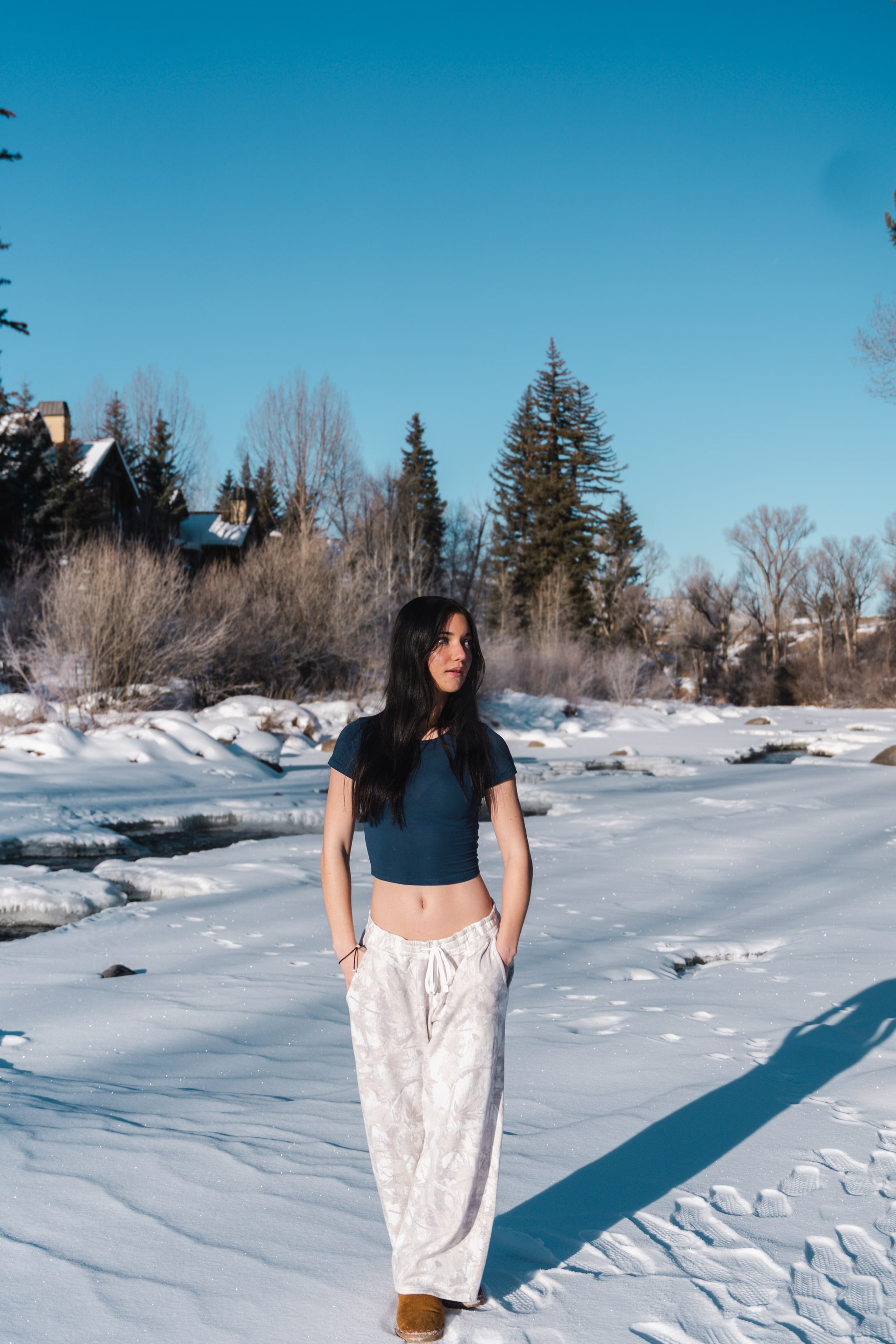 Lucy in a navy top and white skirt standing on a frozen riverbank, long blue shadows