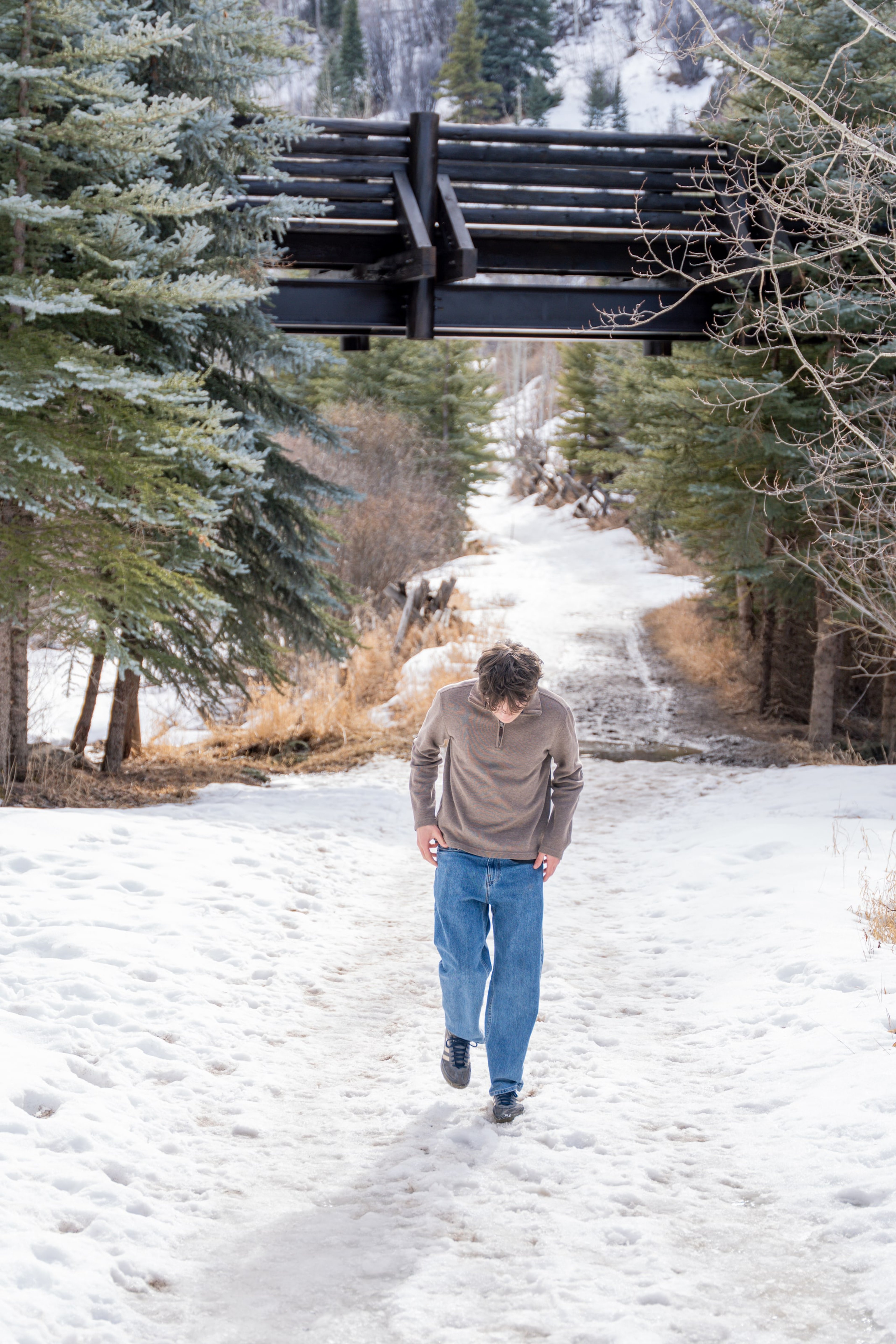 Luca walking away under a timber bridge on a snowy trail