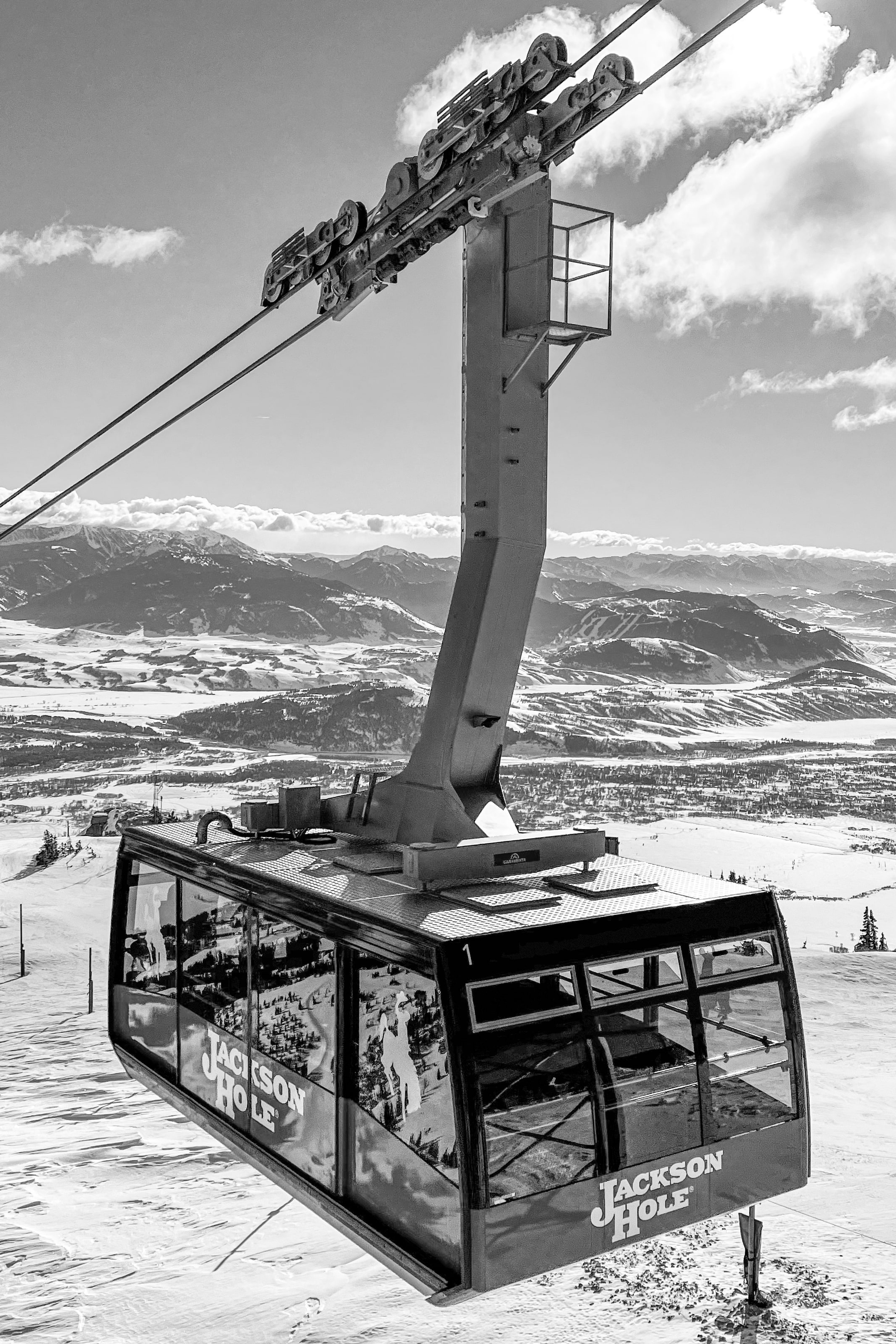 The Jackson Hole aerial tram climbing its cables toward a bright winter sky, in black and white