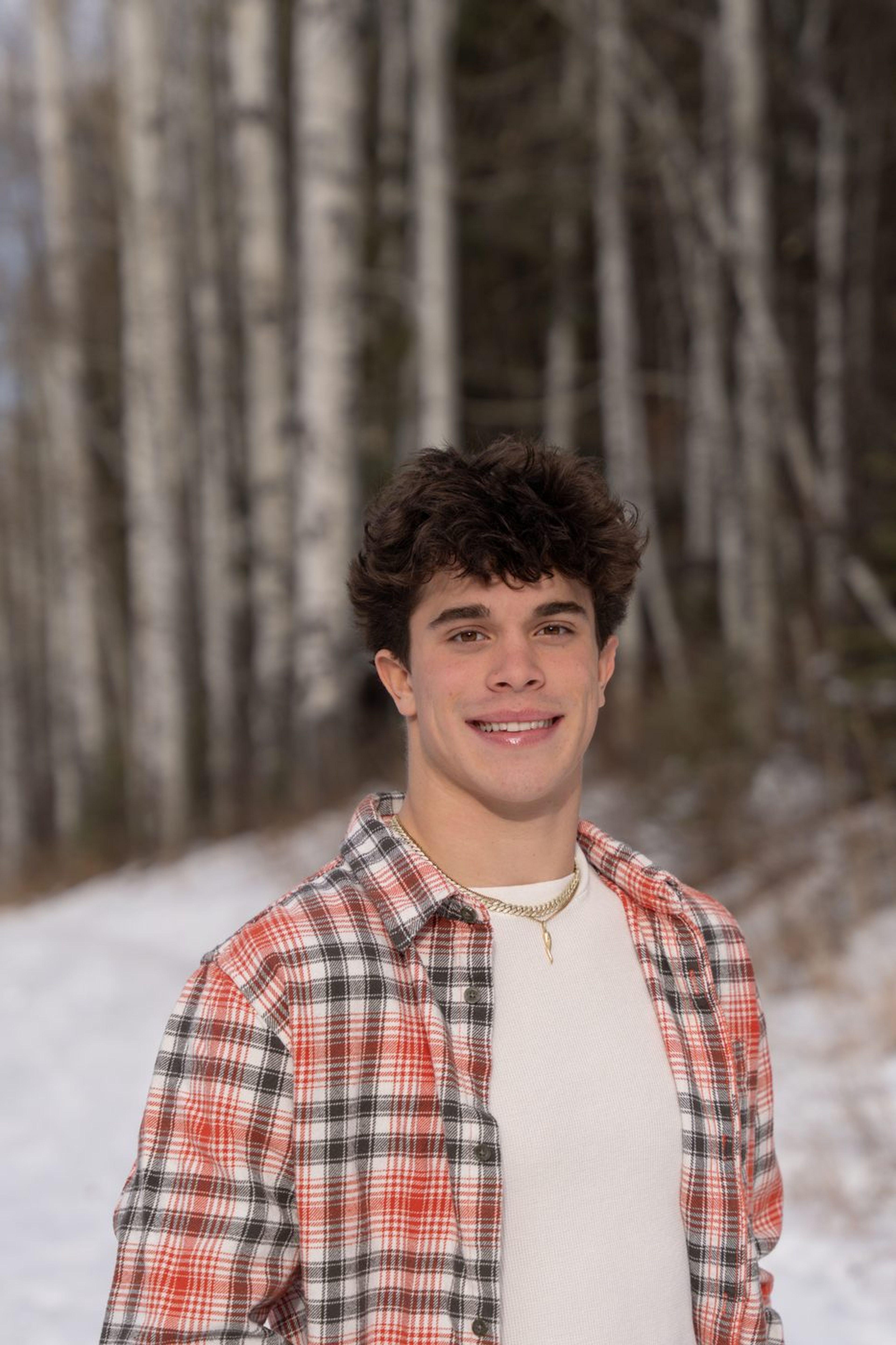 Smiling senior portrait in a plaid flannel before snowy birches