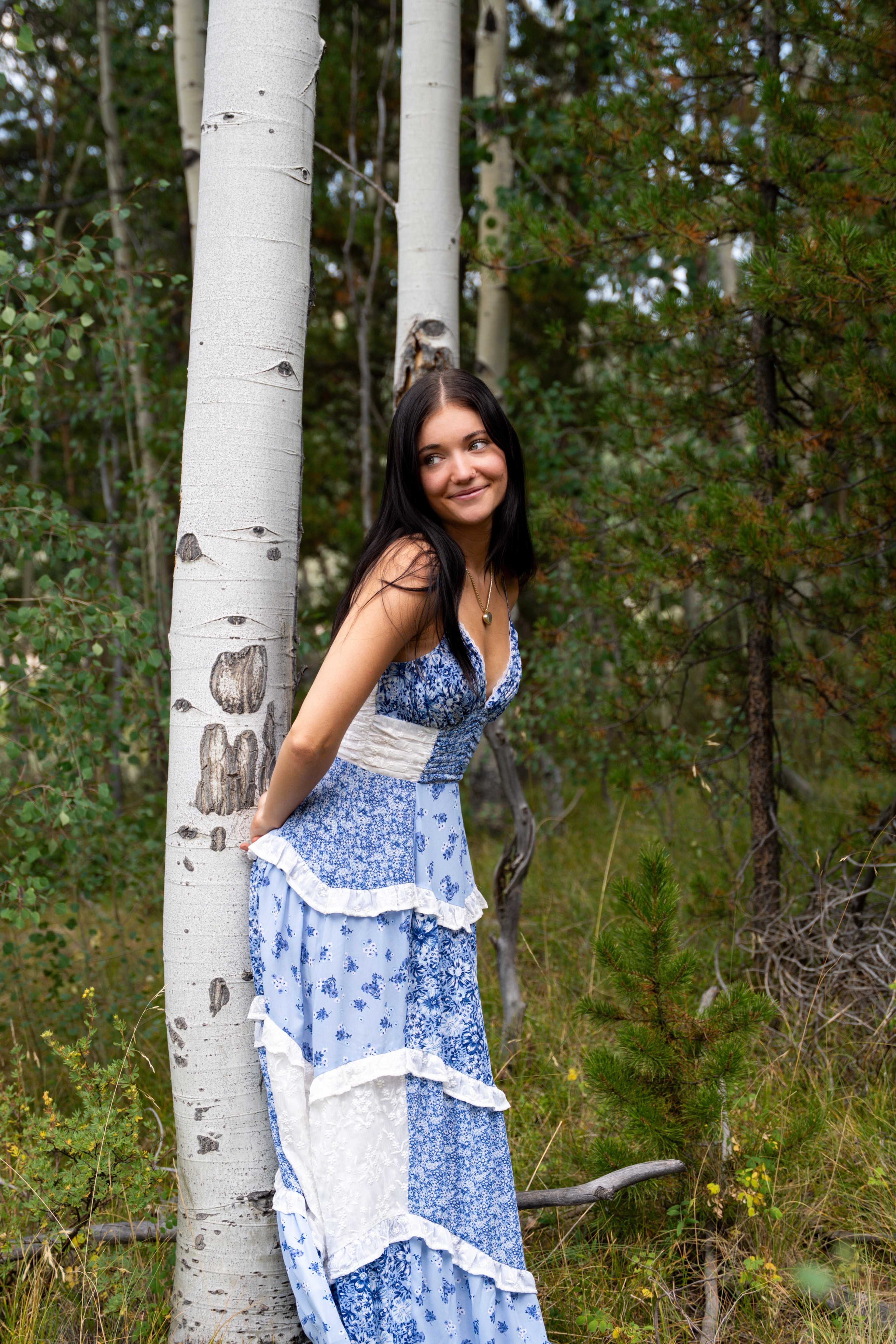 Lucy leaning against a carved aspen trunk in a blue dress