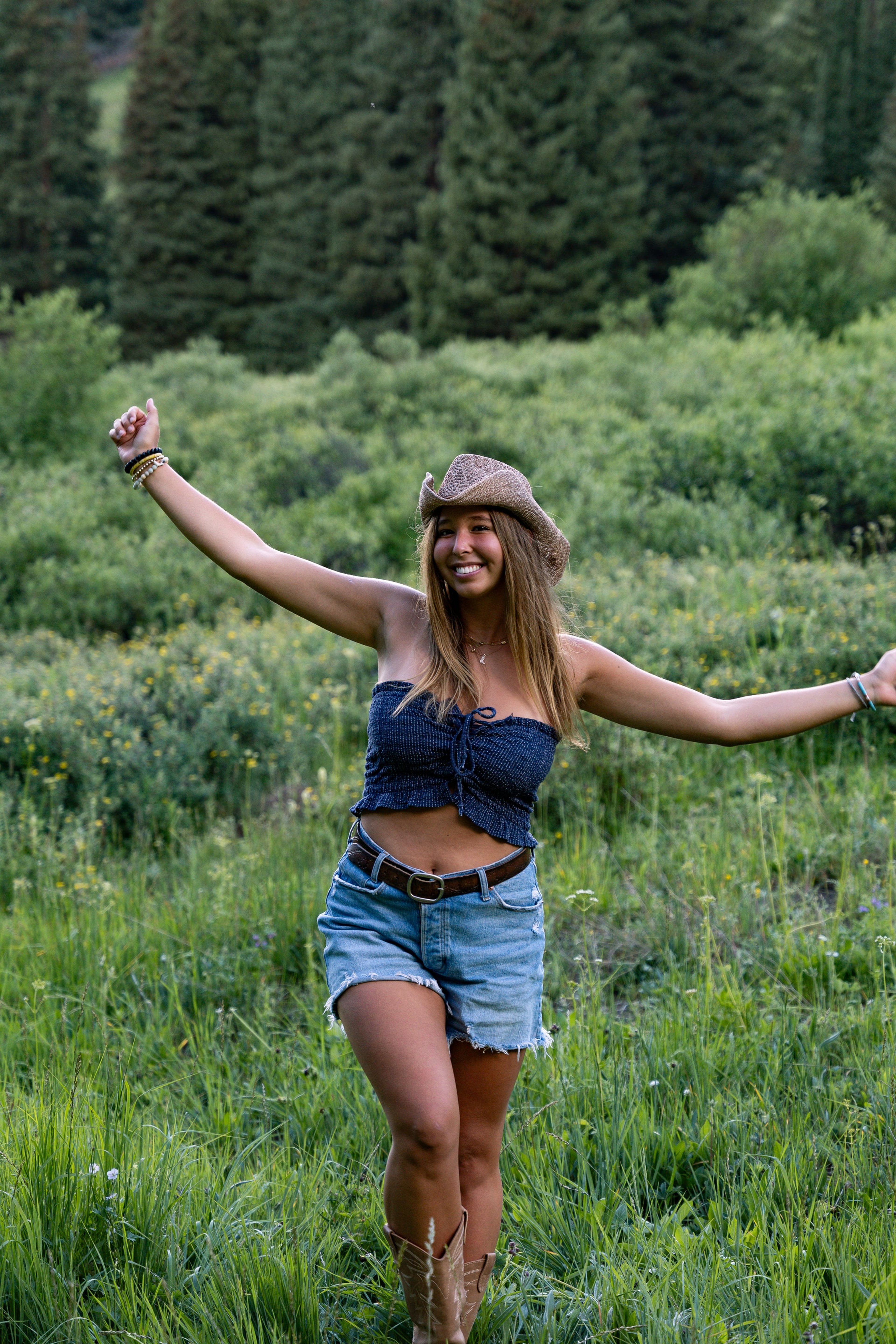 A girl in a cap with arms spread wide on the flower hillside