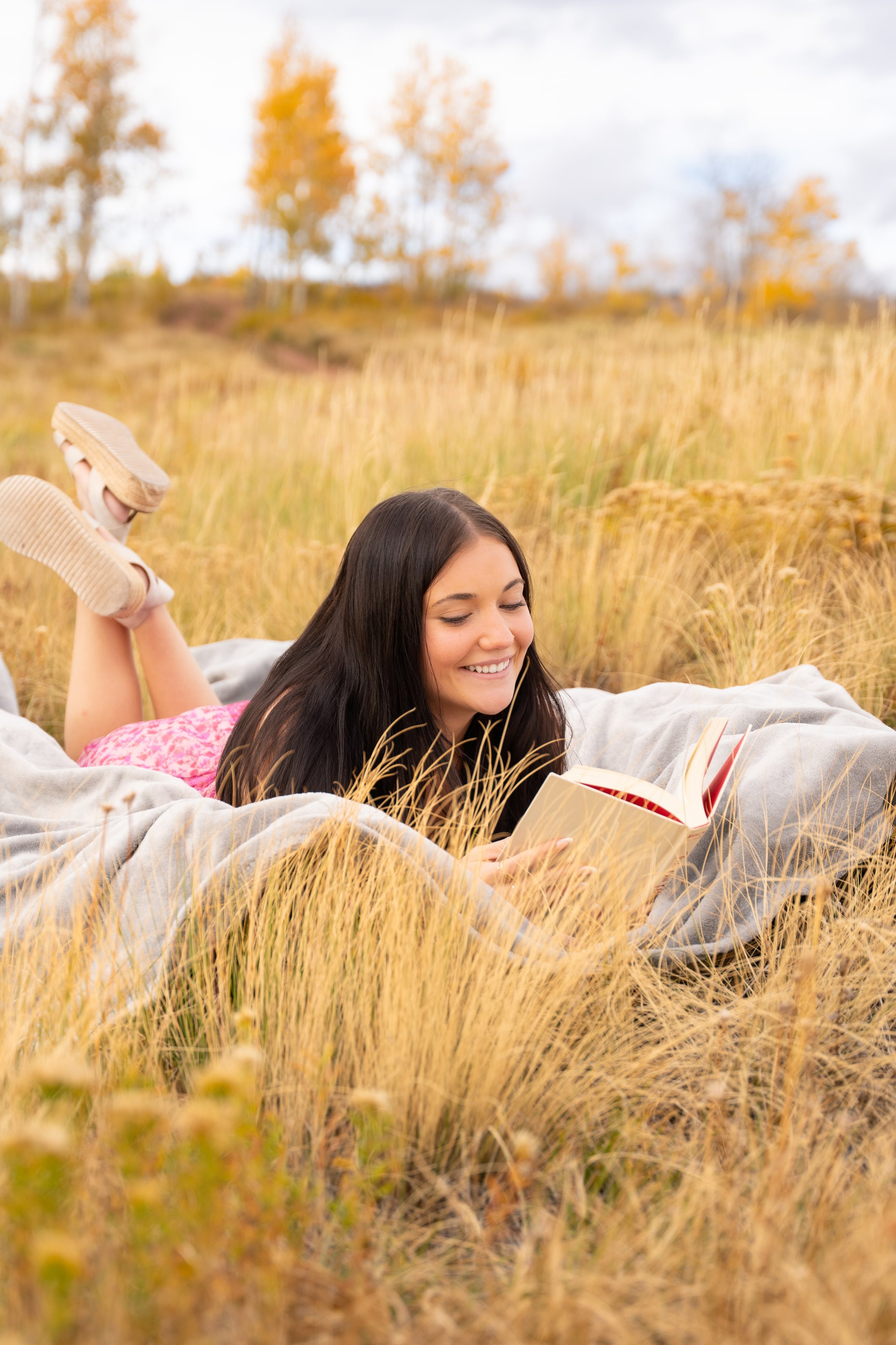 Lucy reading on her stomach in a gold field, boots crossed in the air