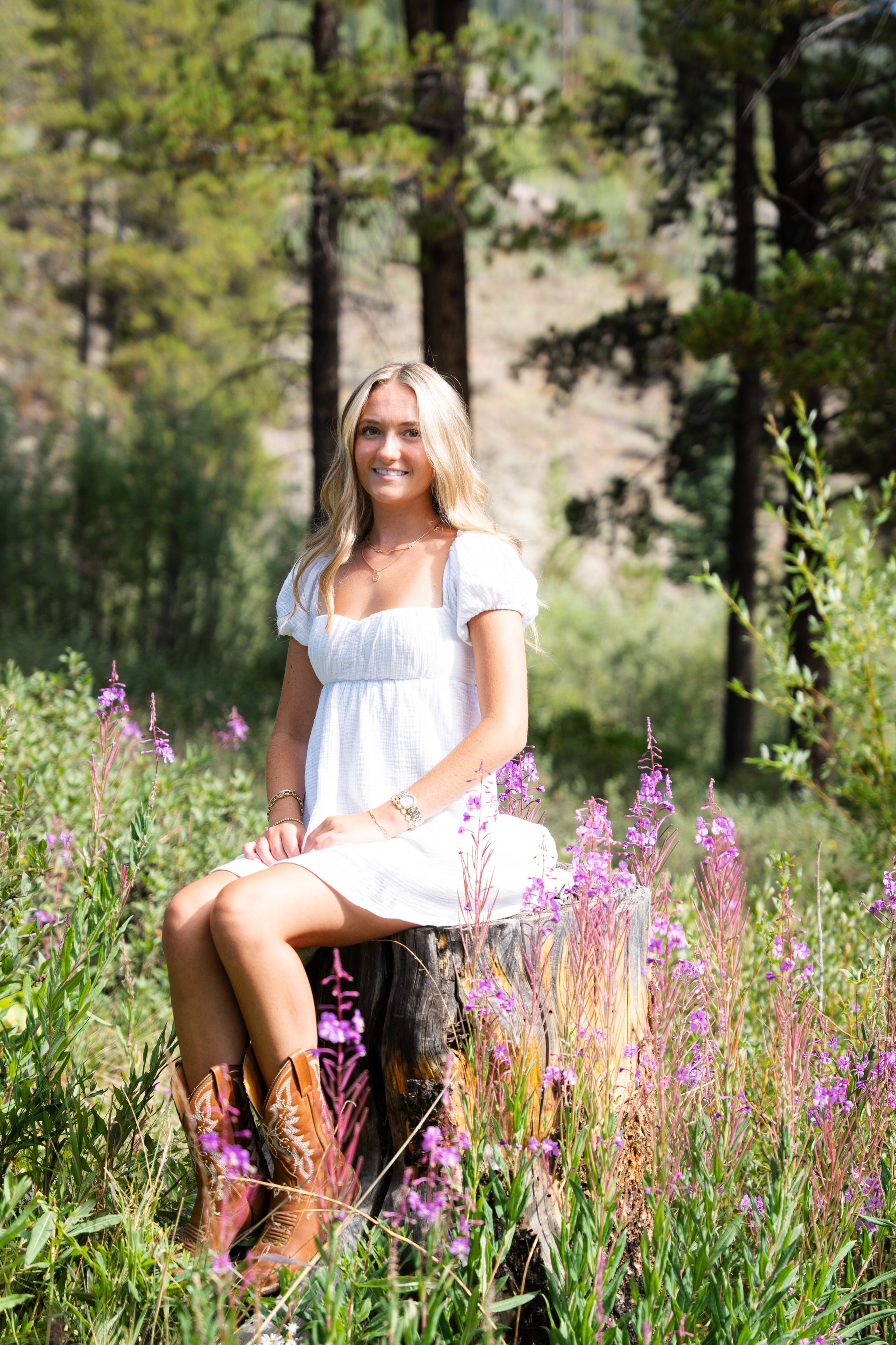 Caleigh seated among pink wildflowers at the edge of a forest