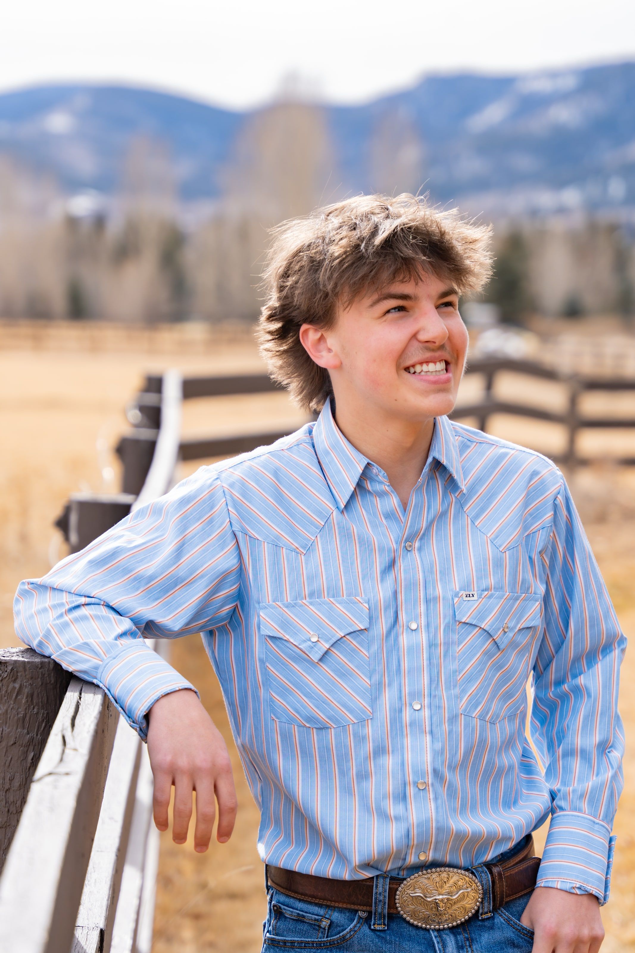 Teagan leaning on a ranch fence in a blue western shirt, smiling