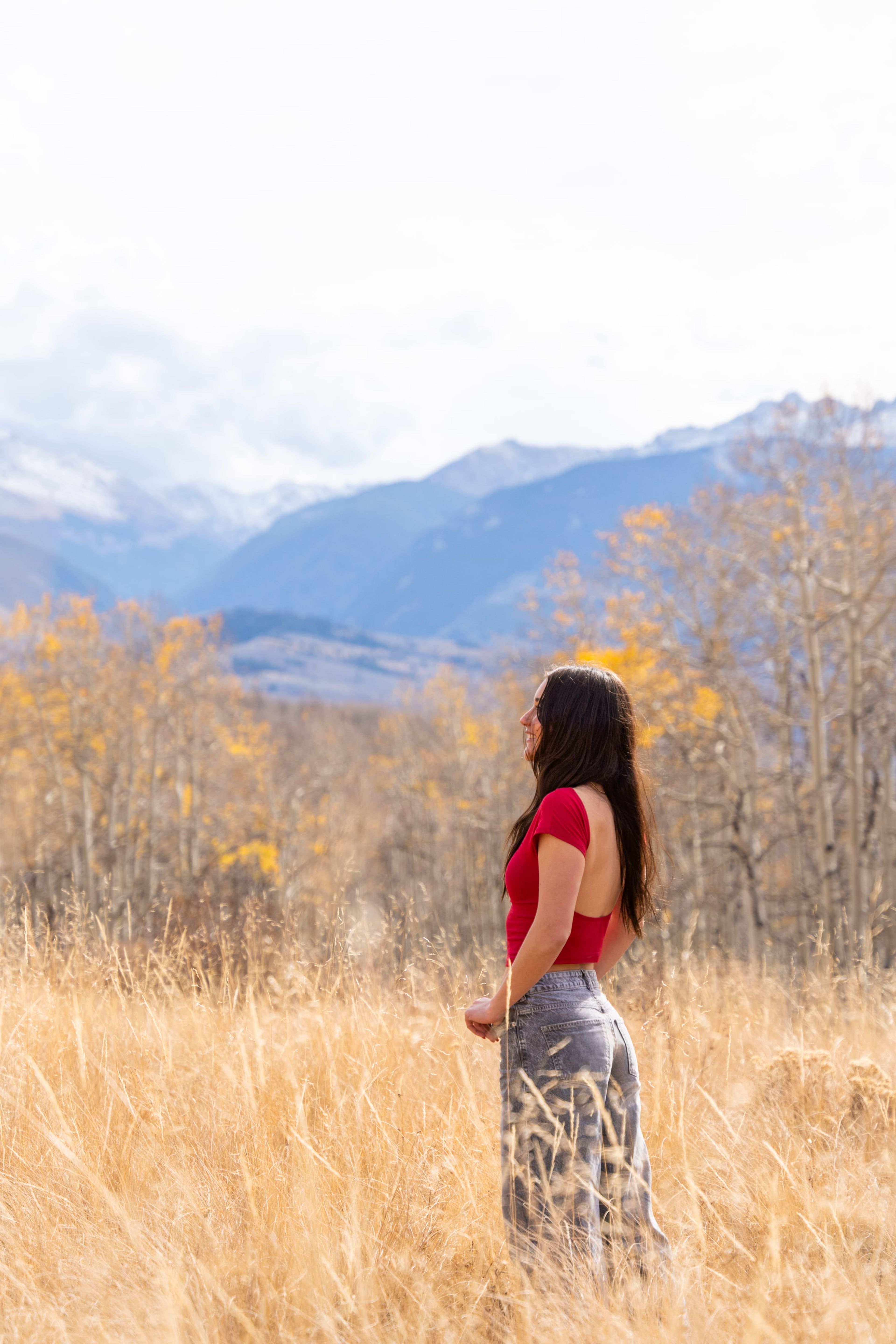 Lucy in red standing in a golden field, snow-capped range on the horizon