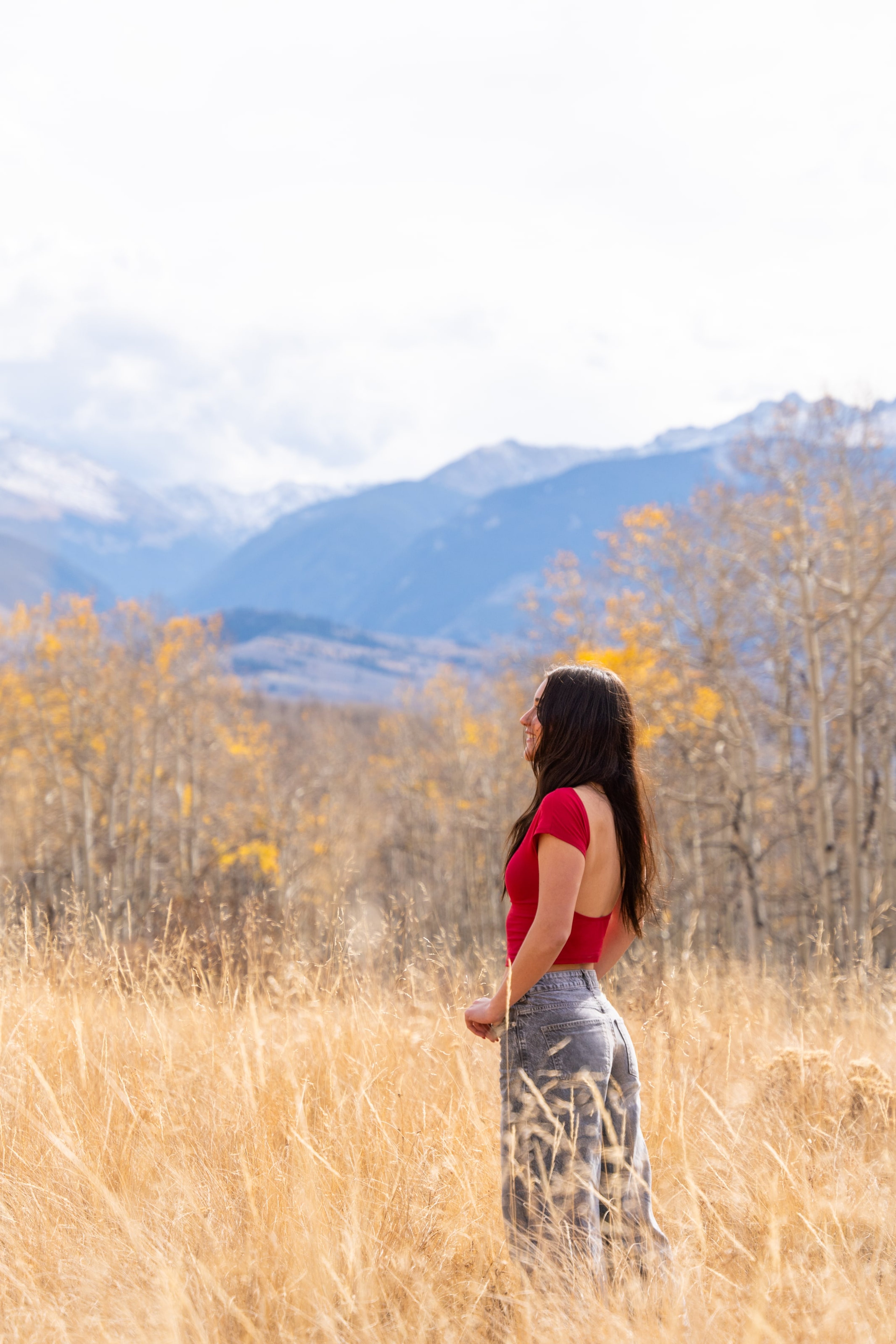 Lucy in red standing in a golden field, snow-capped range on the horizon