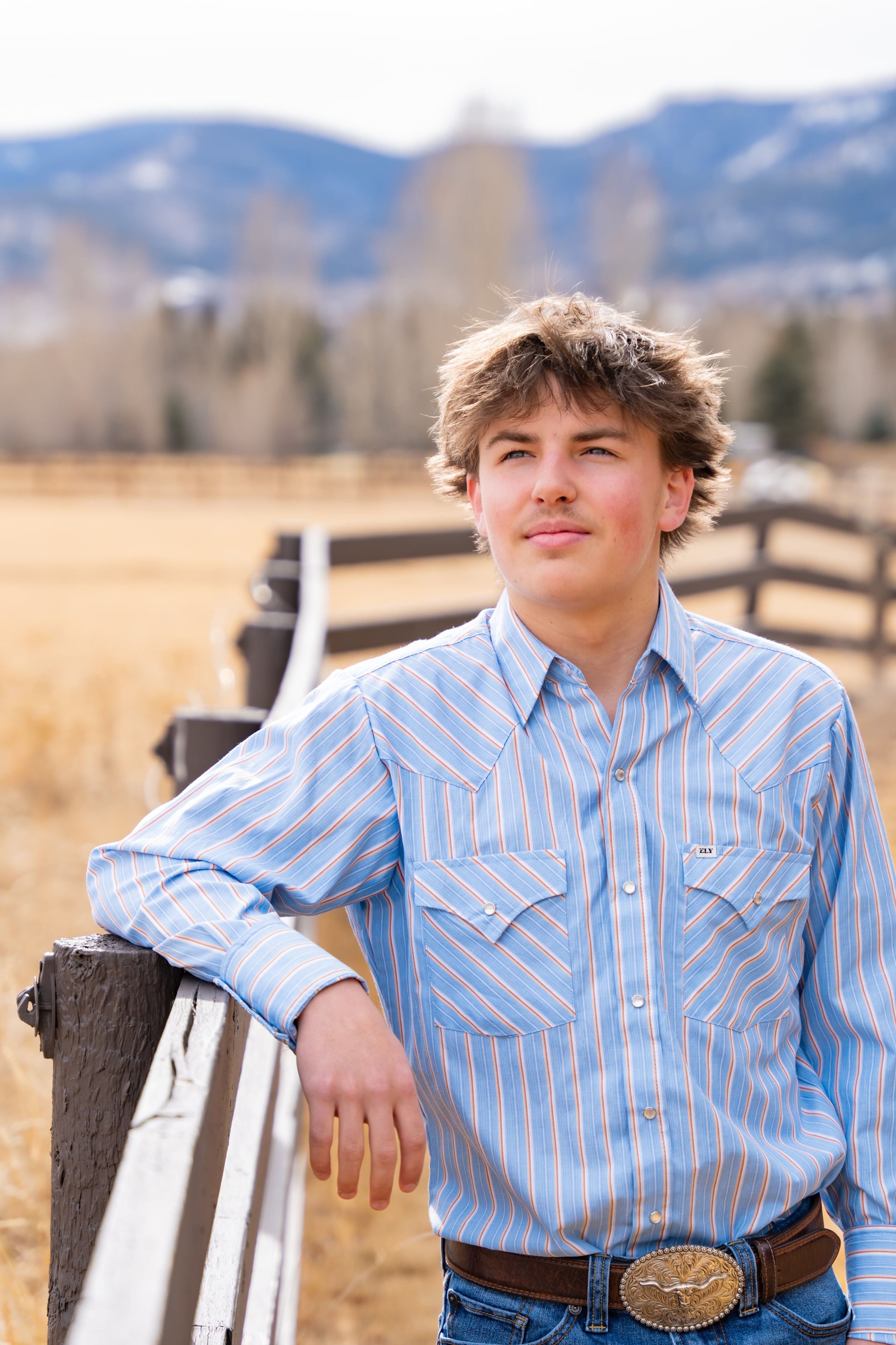 Teagan at the fence, thumb hooked near a rodeo belt buckle