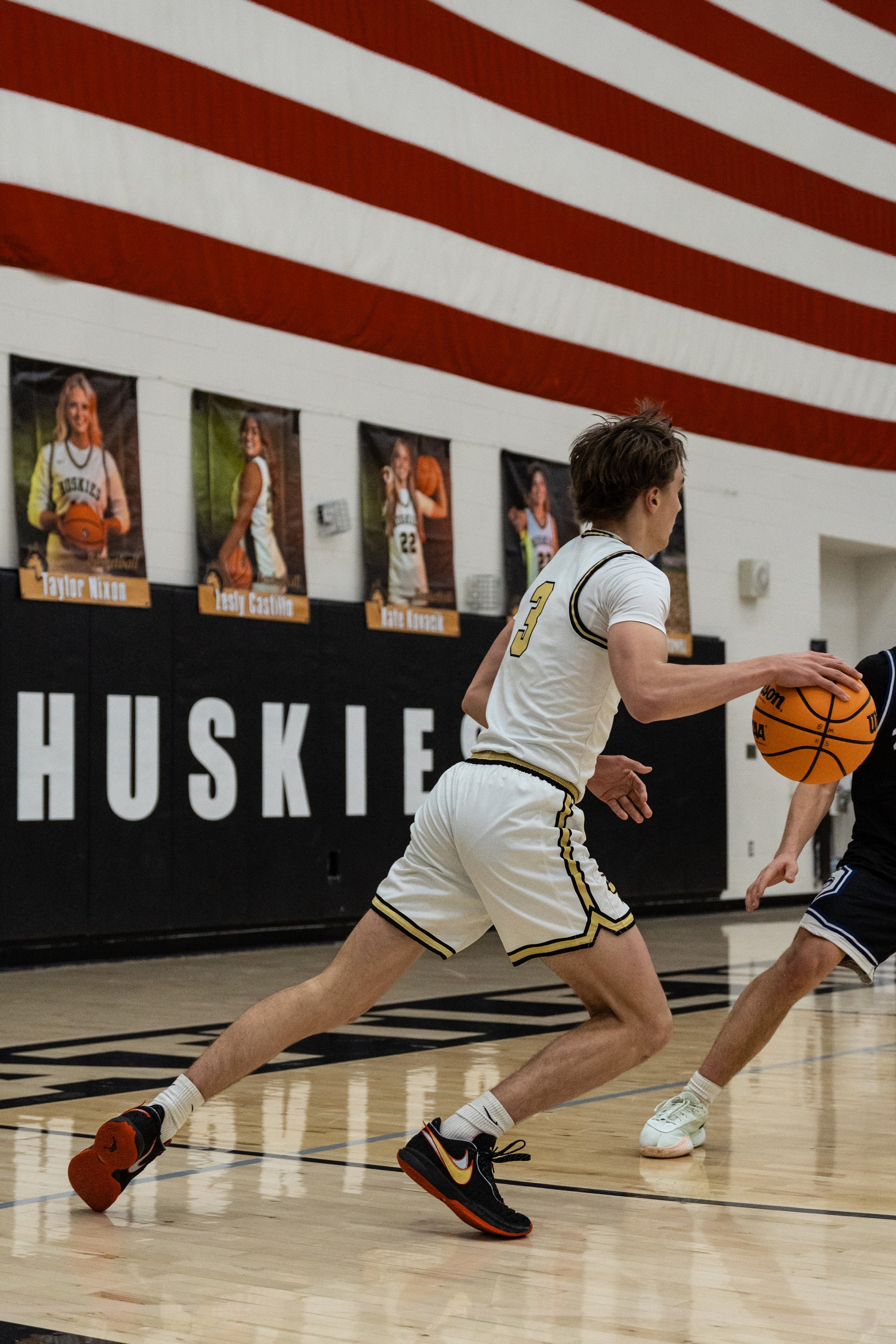 A Huskies player drives along the baseline beneath an American flag