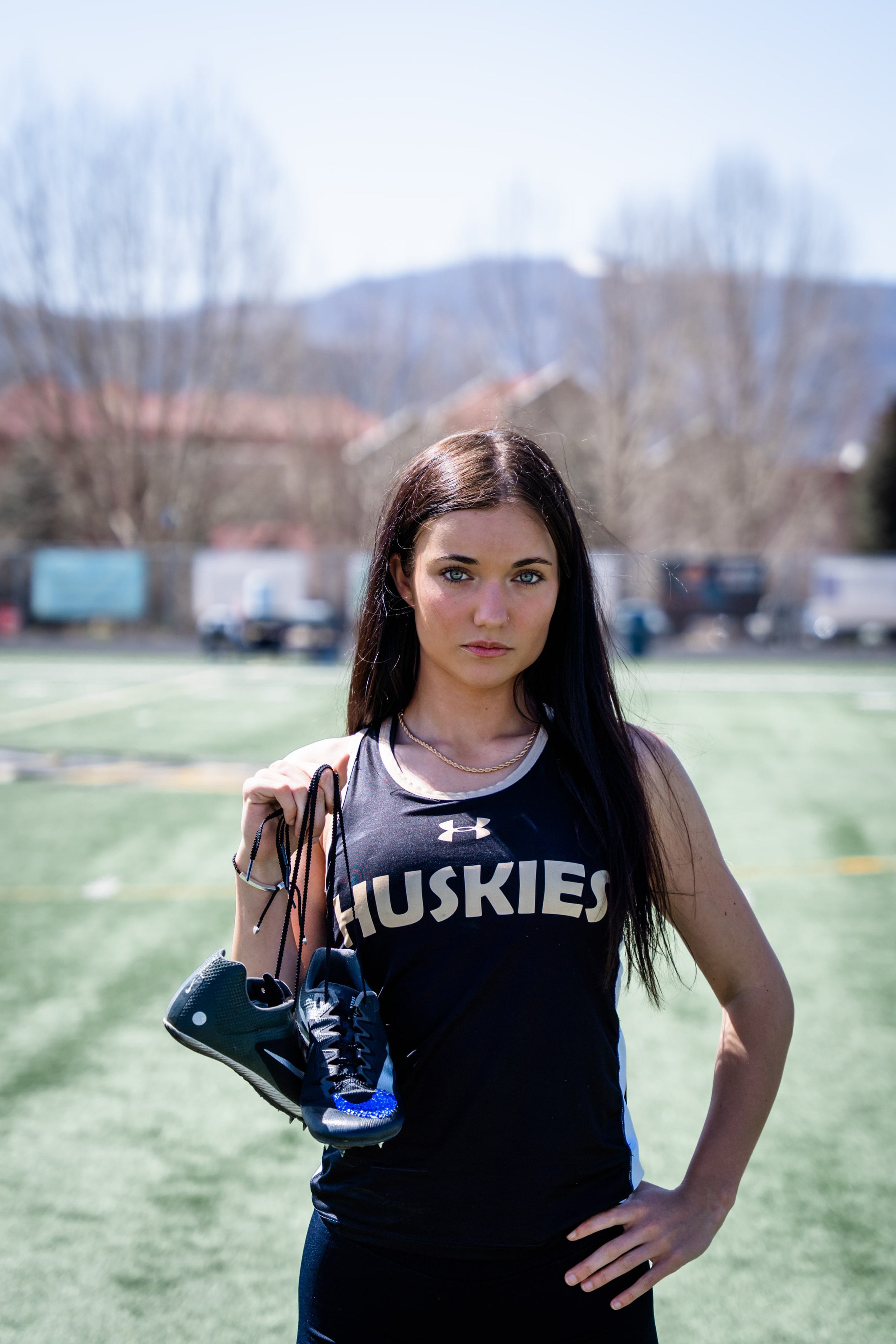 Lucy in a Huskies singlet holding her spikes, facing the light