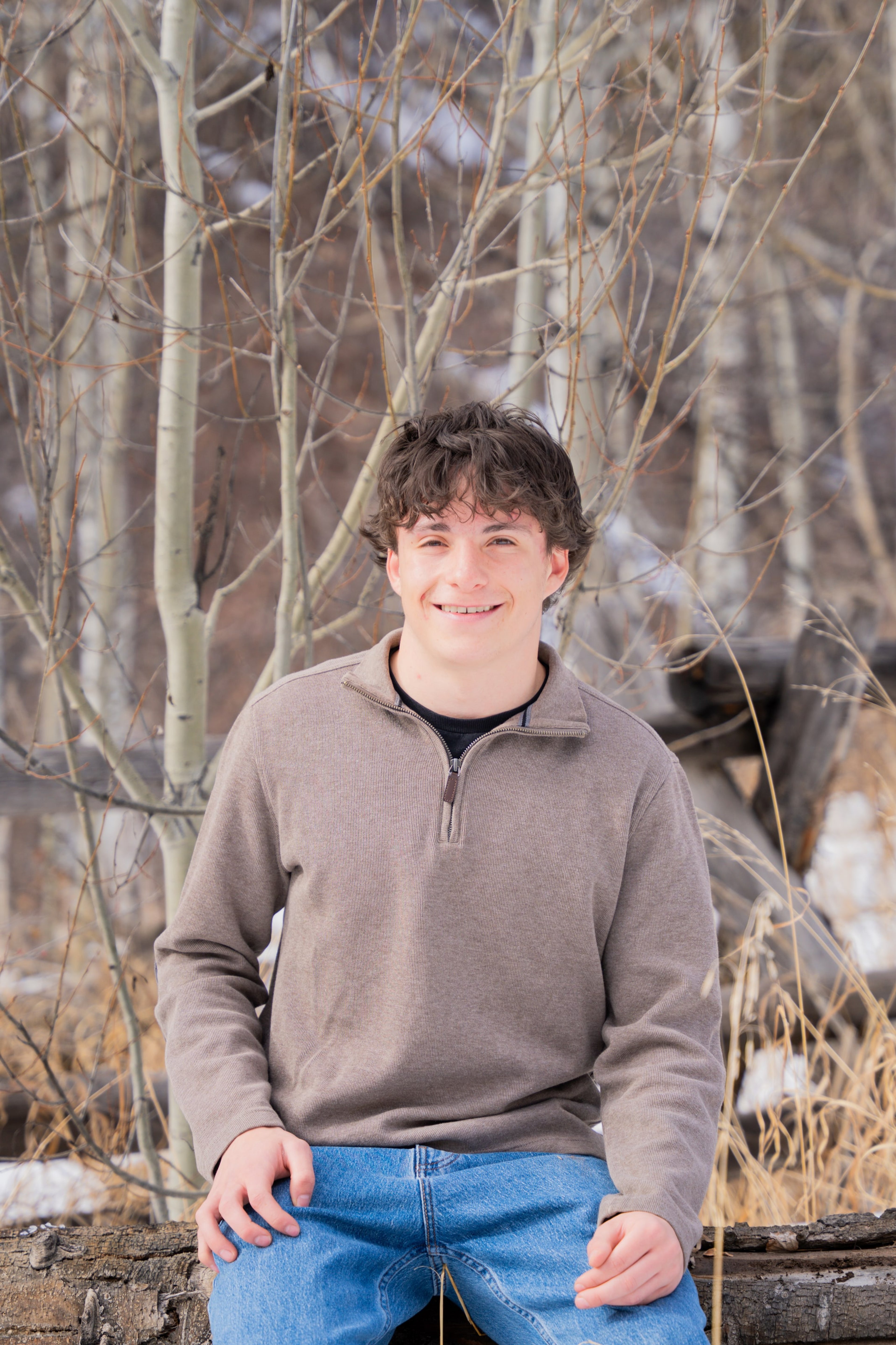 Luca smiling in a brown sweater, aspens behind