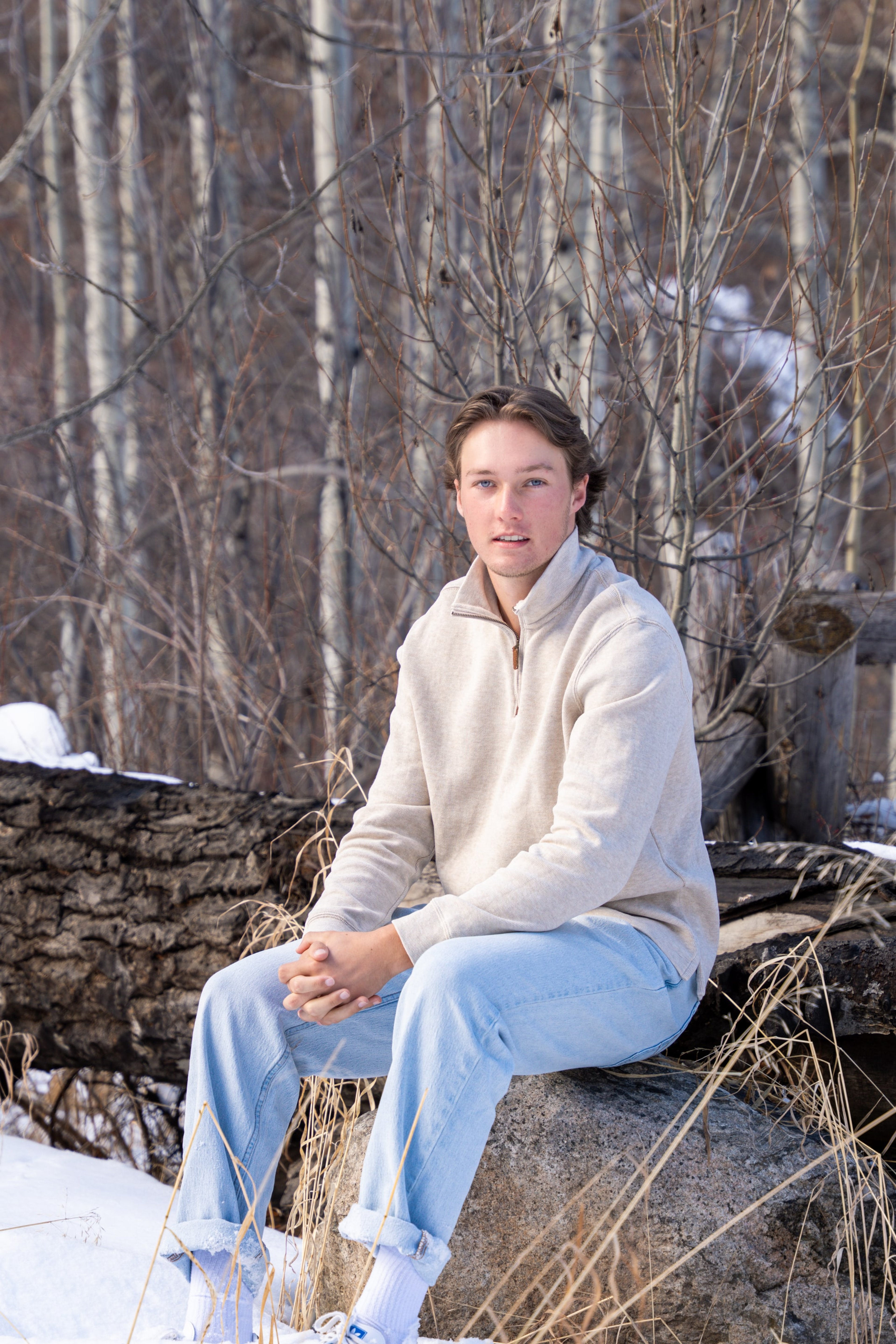 Caeden seated on a stone wall among bare aspens