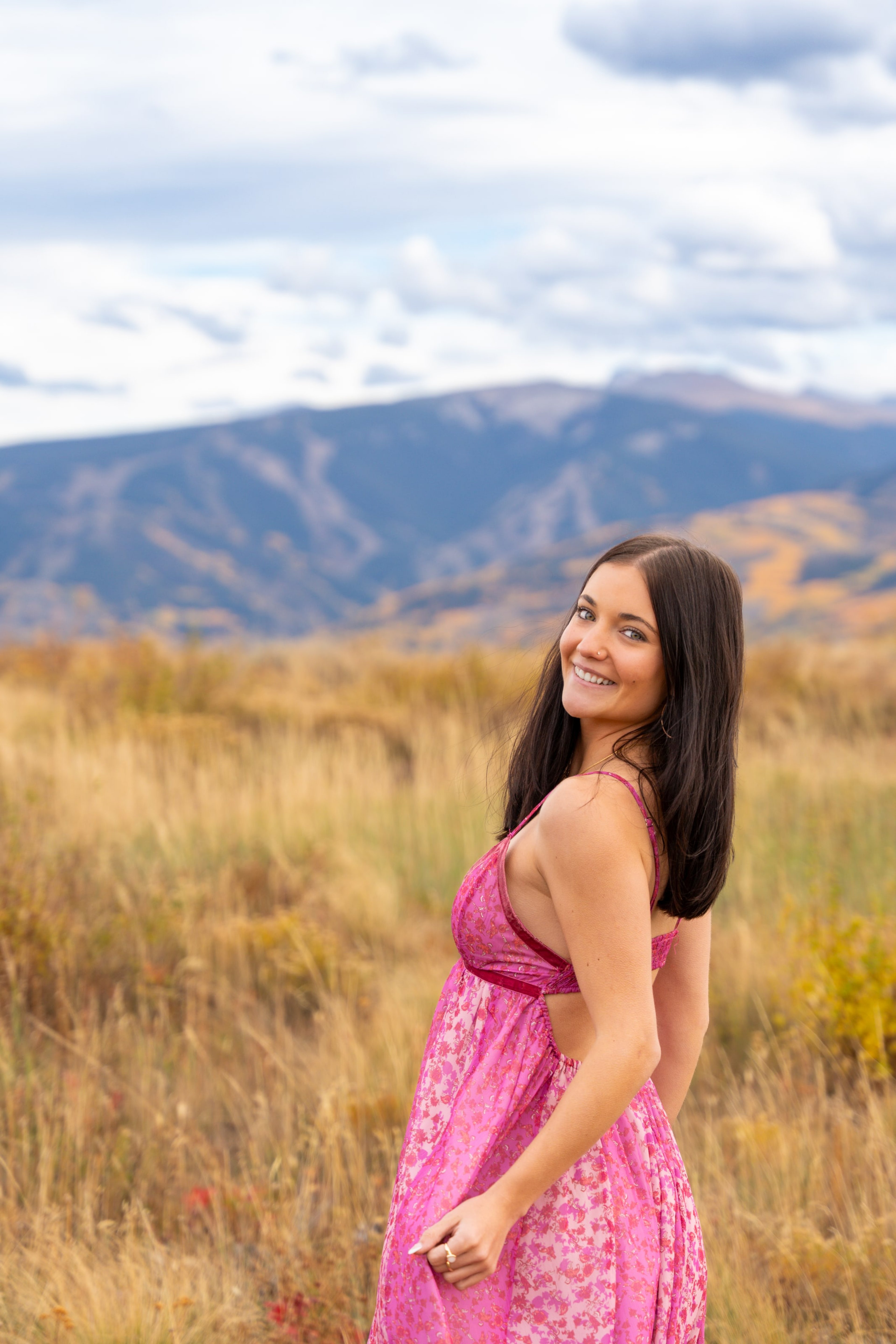 Lucy in a pink dress in a gold autumn field, mountains behind