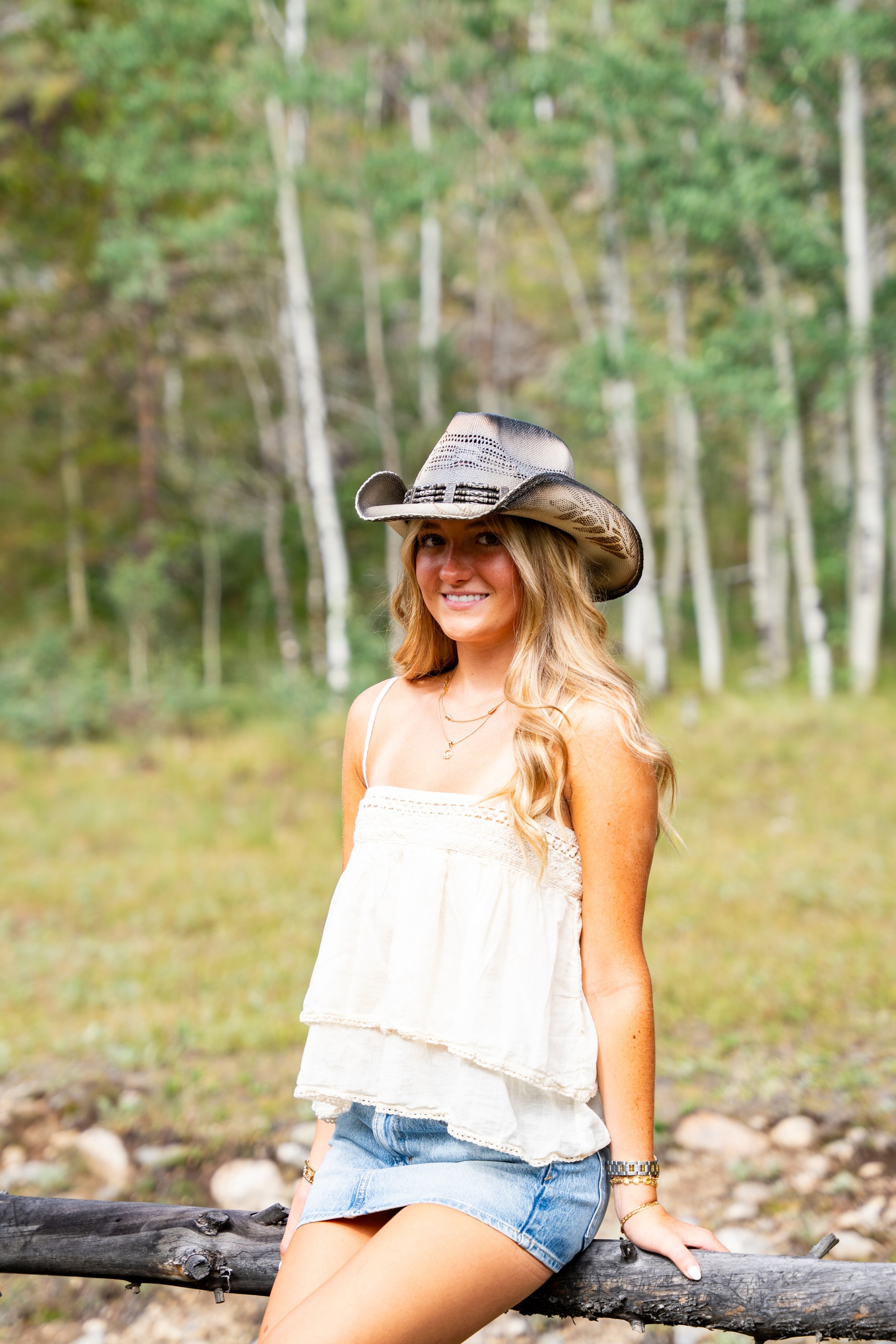 Caleigh wearing a cowboy hat and sitting on a rustic fence