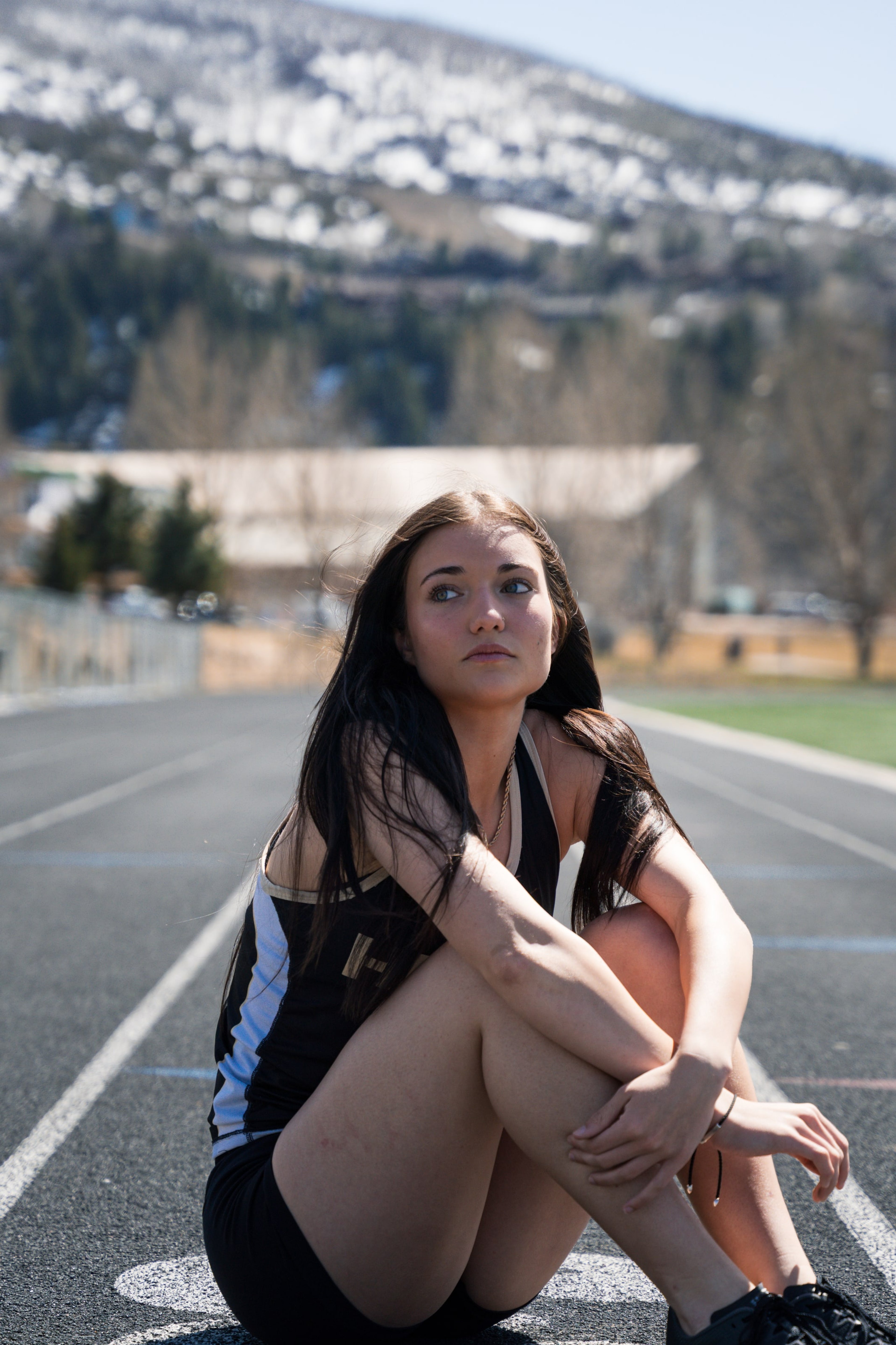 Lucy sitting on the track hugging one knee, looking off