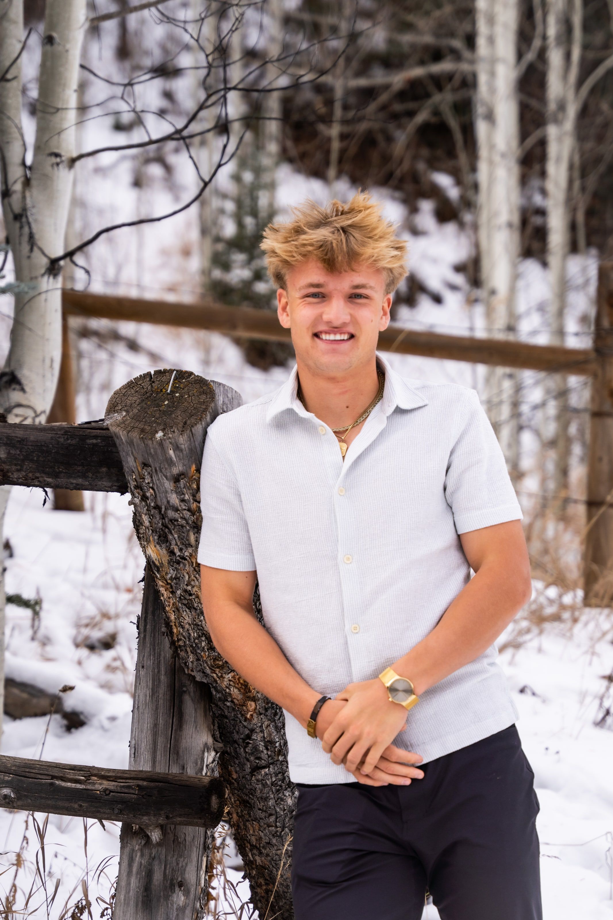 Jakob leaning on a fence post in a white shirt, smiling
