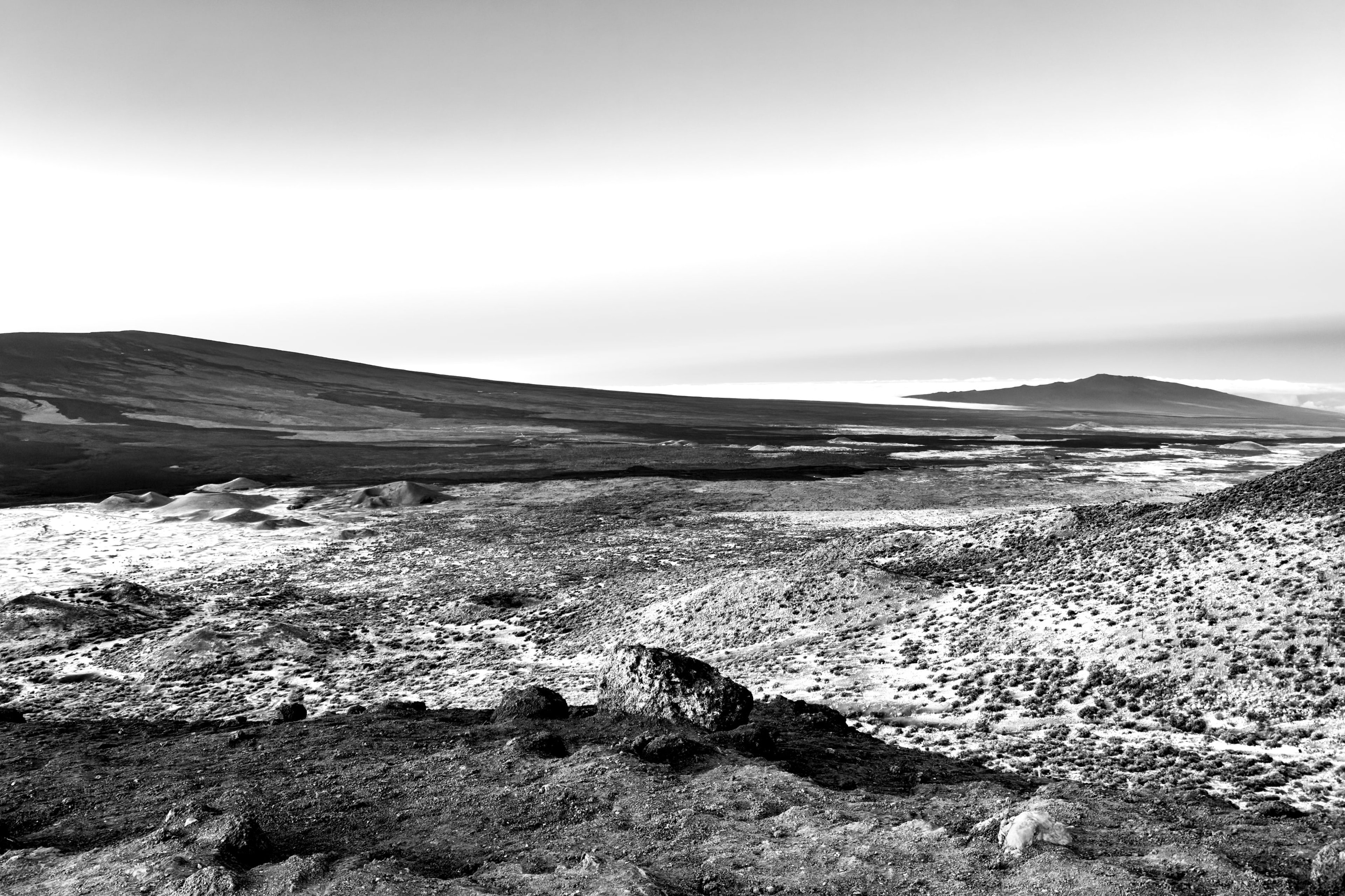 A barren volcanic slope meeting a wide horizon under streaked clouds, in black and white