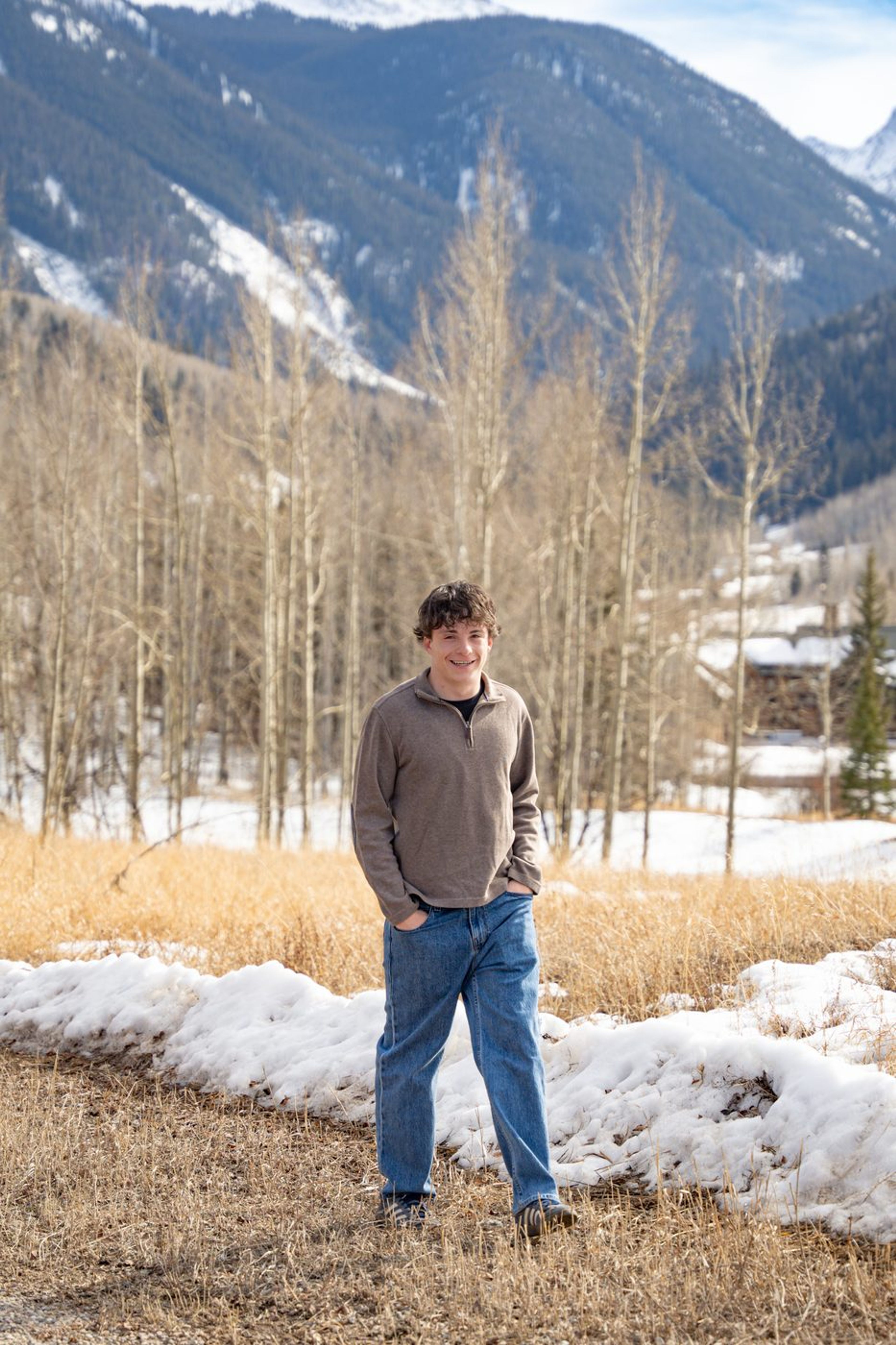Senior portrait in a quarter-zip among snowy mountains and bare aspens