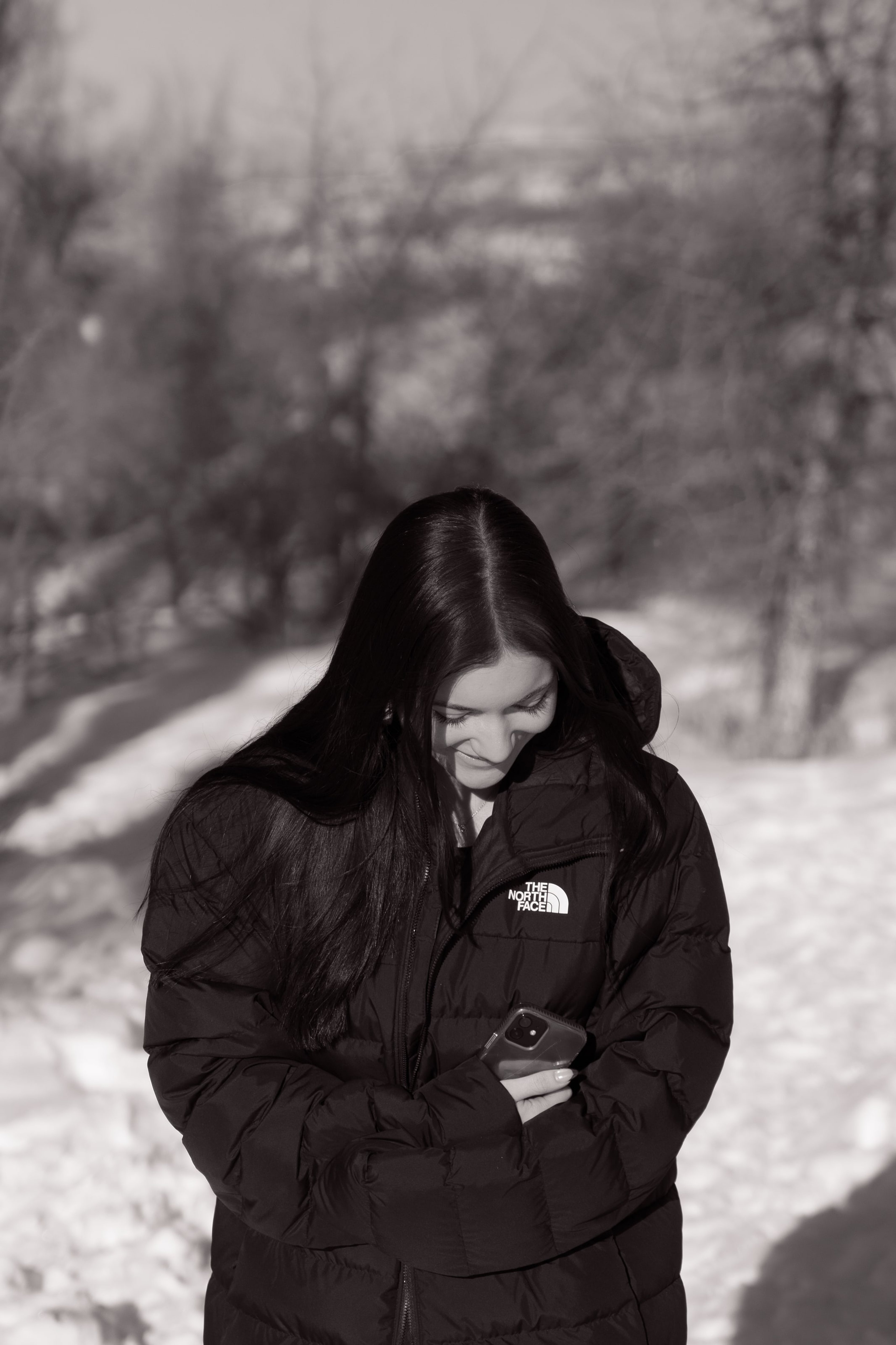 Lucy in a black puffer looking down at a camera in her hands, in black and white