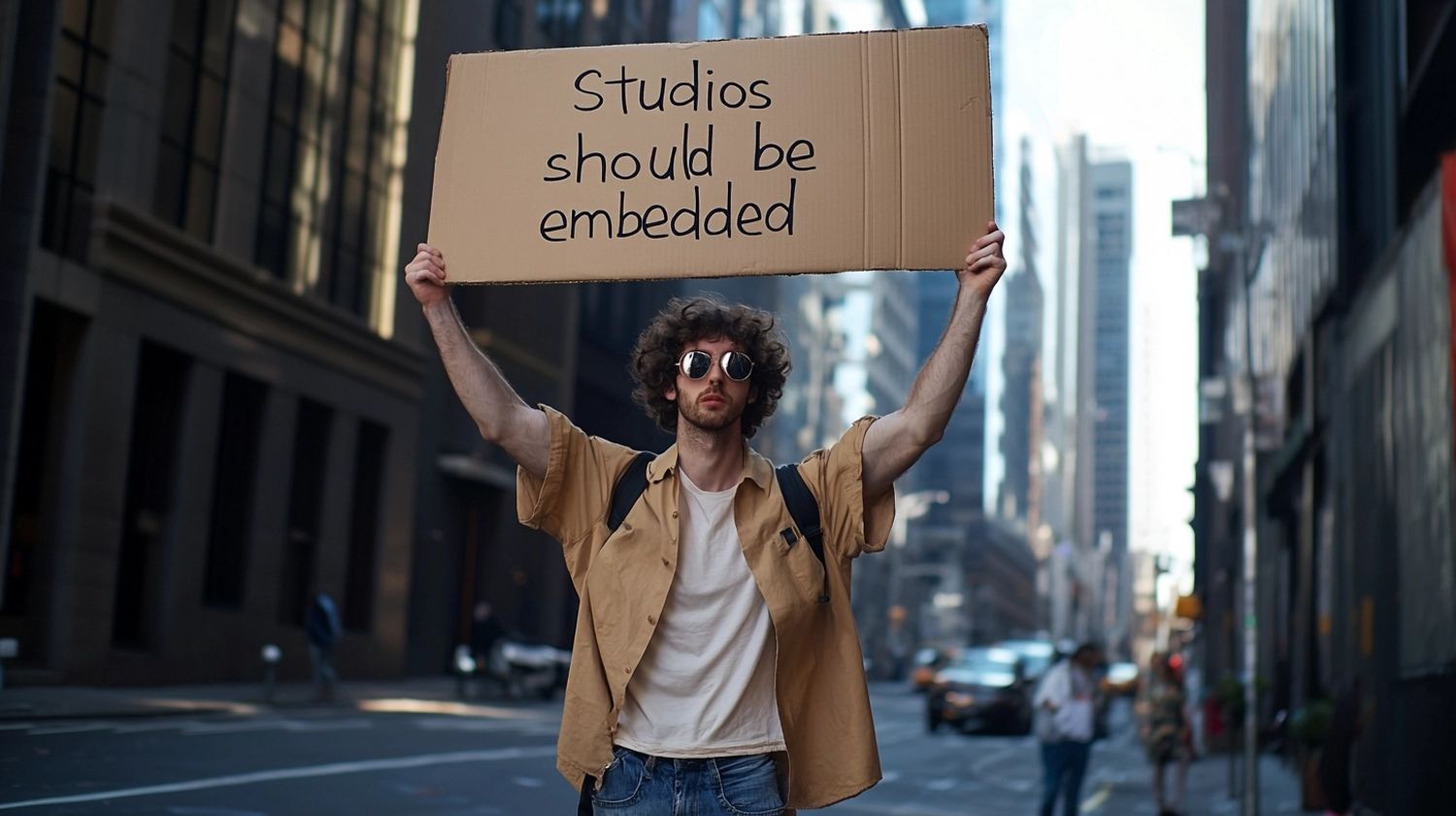 28-year old male with curly hair wearing sunglasses holding a cardboard sign high above his head with the text "Studios should be embedded" on the streets of New York, Hasselblad