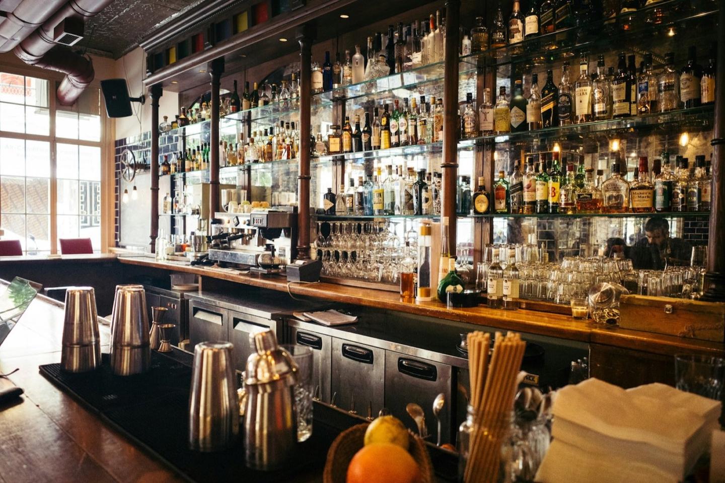 A tall back bar lit warm, shelves of bottles rising to the ceiling.