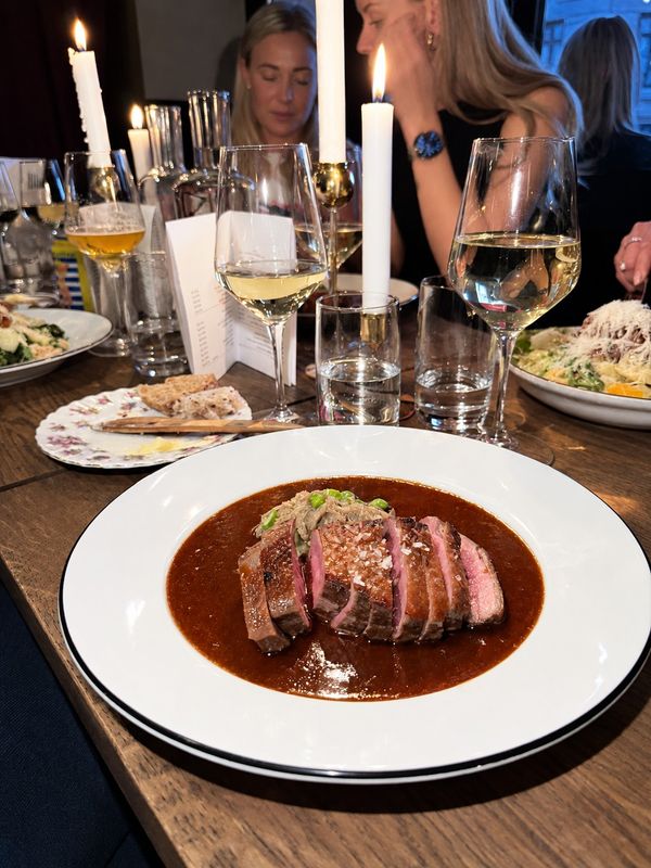 Skivat kött i mörk sås på vit tallrik vid ett dukat bord, Bistro Breve