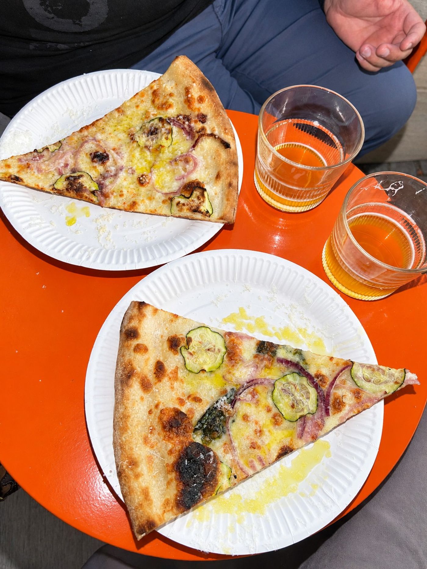 Två pizzaslices på papptallrikar med öl på ett orange bord, Bennys Slice Shop